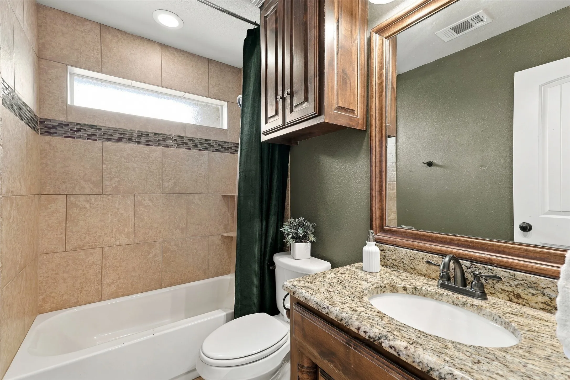 Secondary Bathroom: Full bathroom features a granite countertop, wood cabinetry, tiled tub and shower surround, and decorative accent tile.