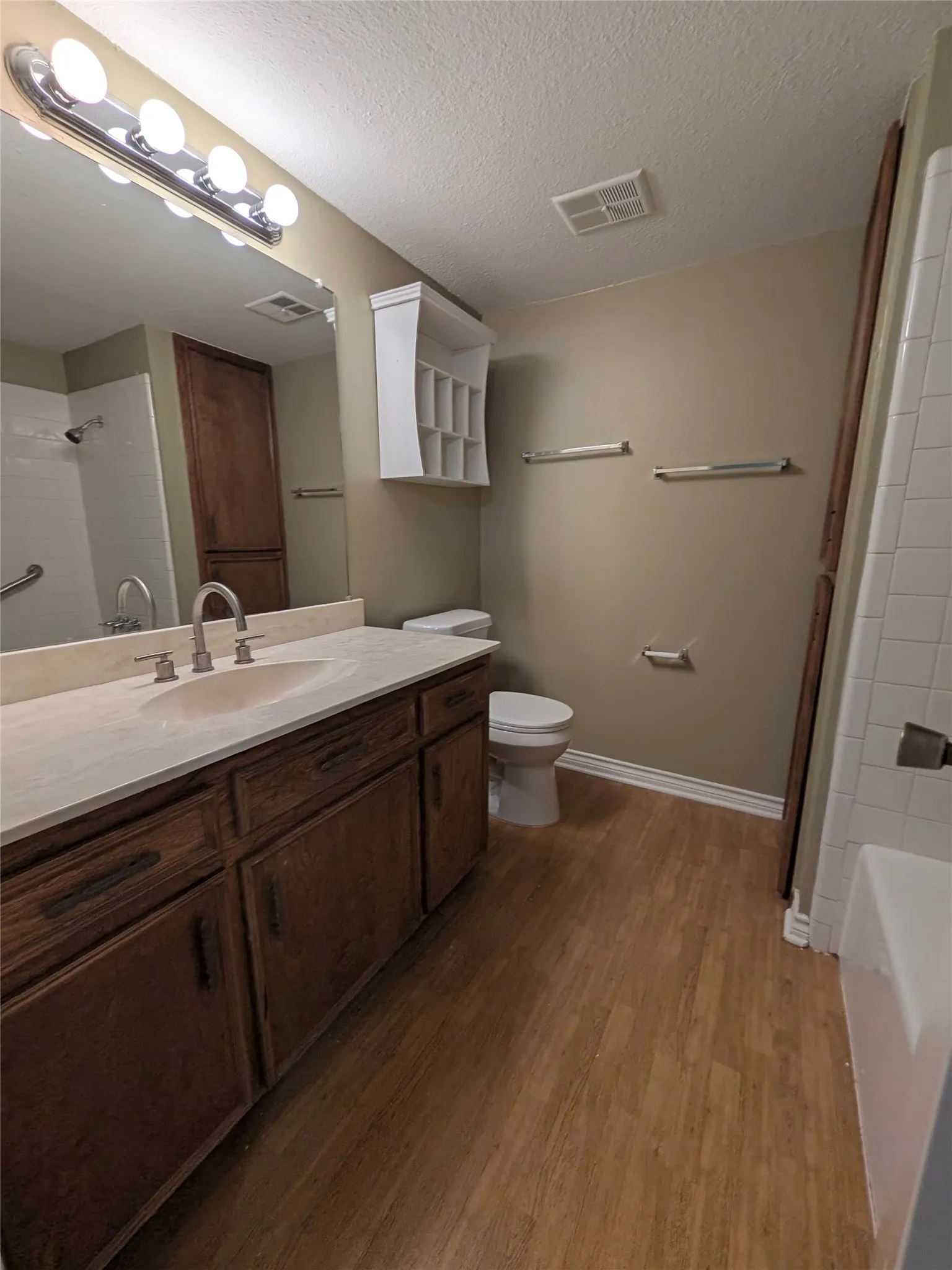 Wood-finish flooring, a vanity with an integrated sink and base cabinetry, a wall-mounted medicine cabinet, and a tiled shower/tub combination