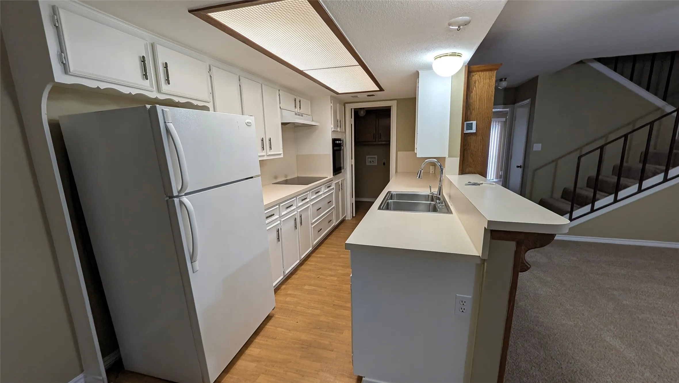 Kitchen featuring white cabinetry, light countertops, wood-finish flooring, and a stainless steel double basin sink