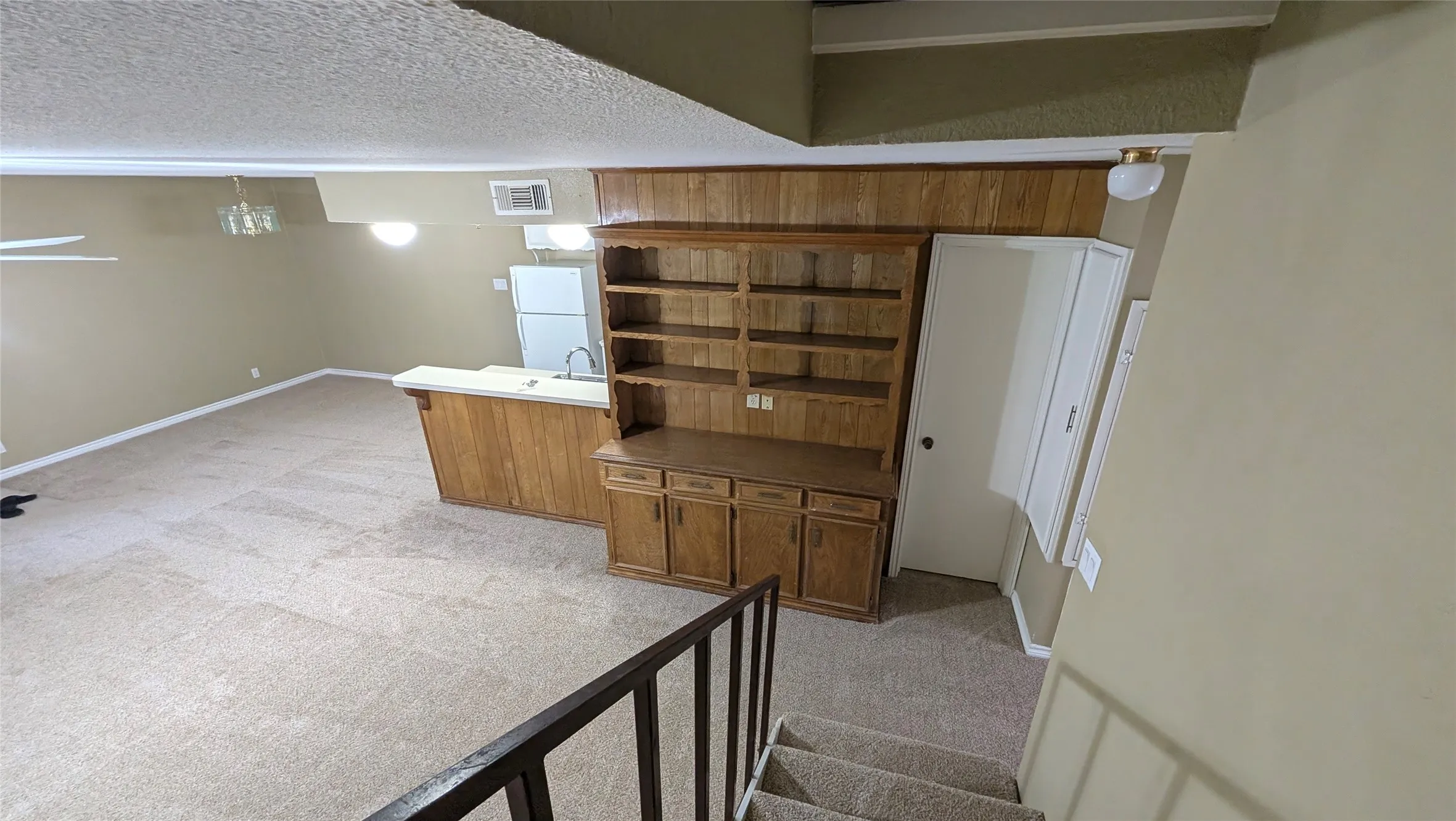 Built-in wooden shelving unit, wood-finish paneling, white kitchen appliances, and a kitchen island with a sink