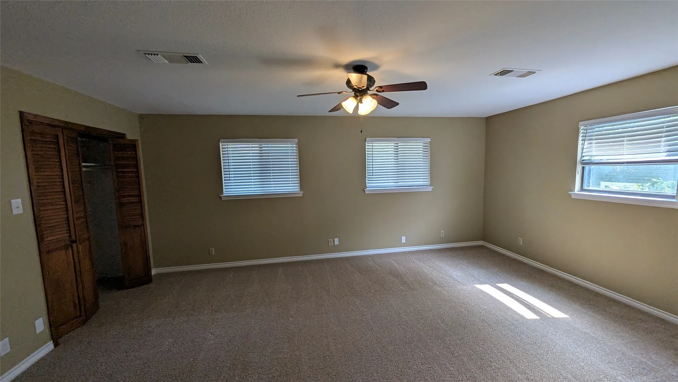 Spacious room with carpet flooring, three windows, a ceiling fan, and bi-fold louvered closet doors