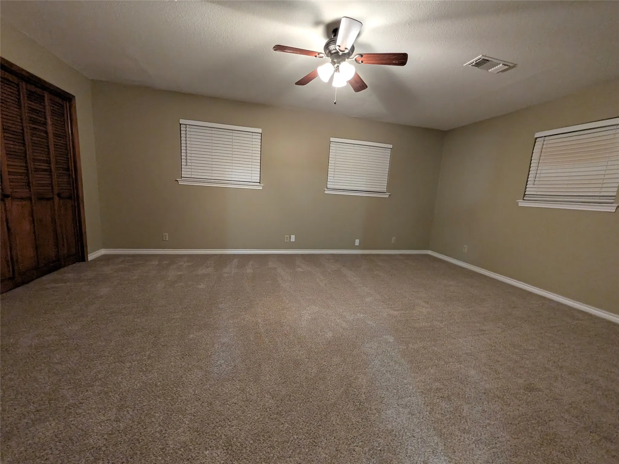 Spacious room featuring neutral carpeting and multiple windows with blinds