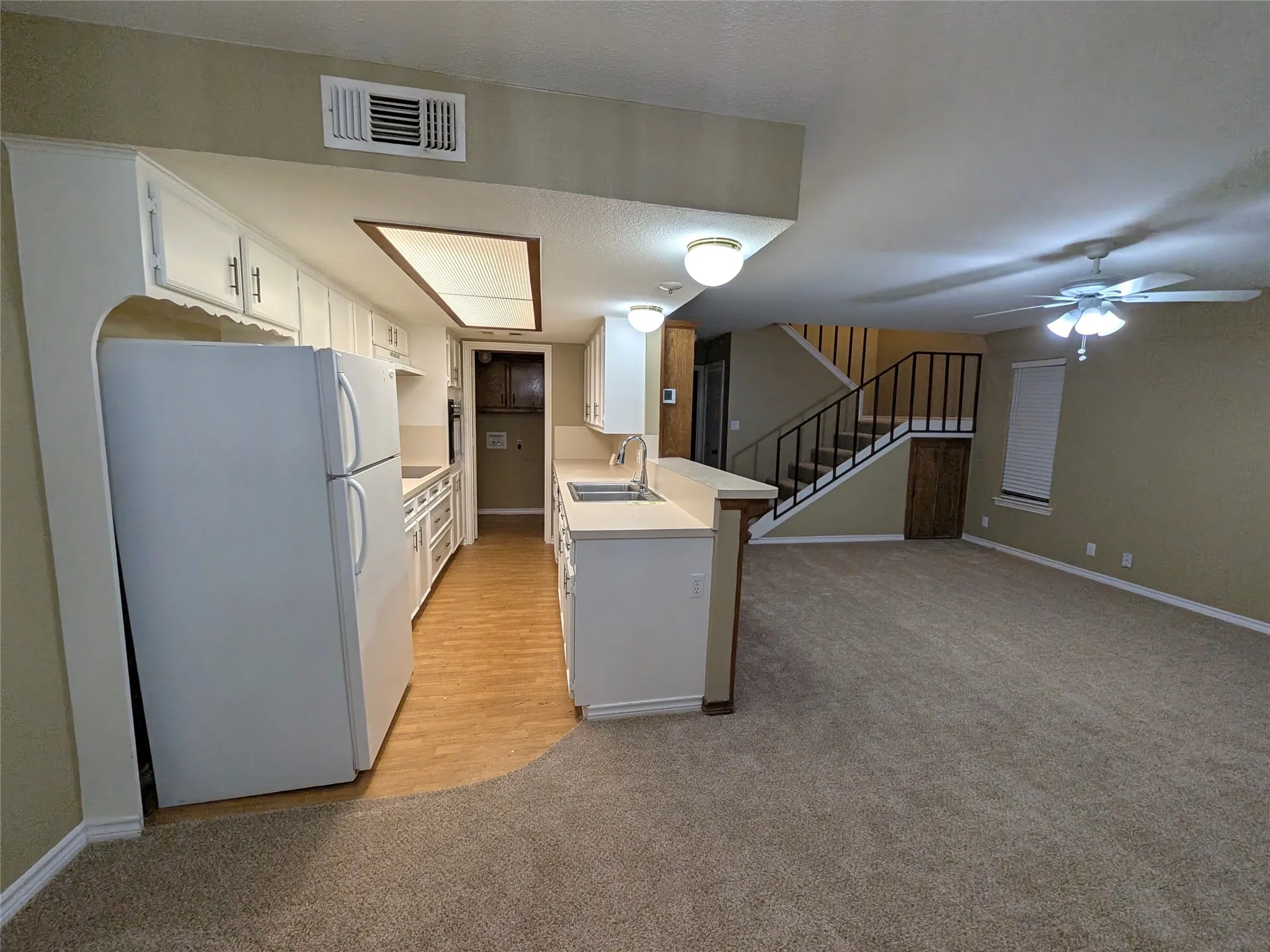 Kitchen with white cabinetry and laminate countertops, featuring a stainless steel sink and wood-finish flooring
