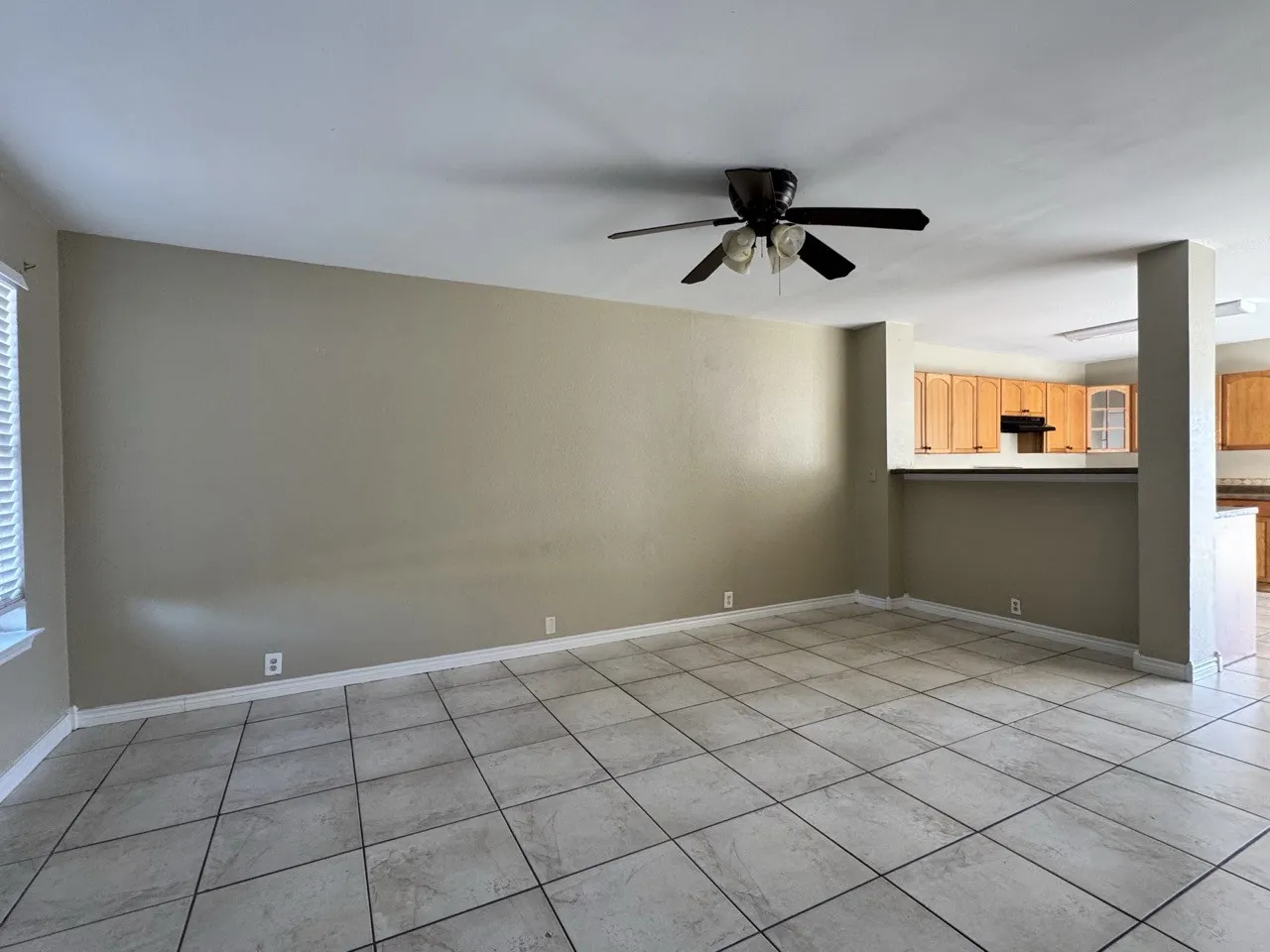 Spacious room featuring neutral tone walls, tile flooring, and a ceiling fan with integrated lighting