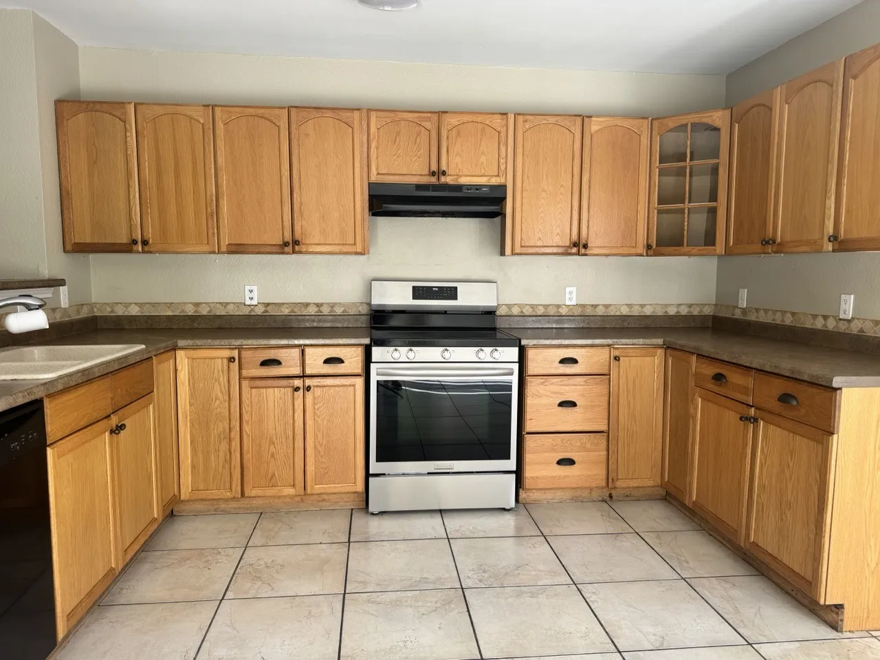 U-shaped kitchen layout featuring light wood-finish cabinetry, a stainless steel range, and tile flooring