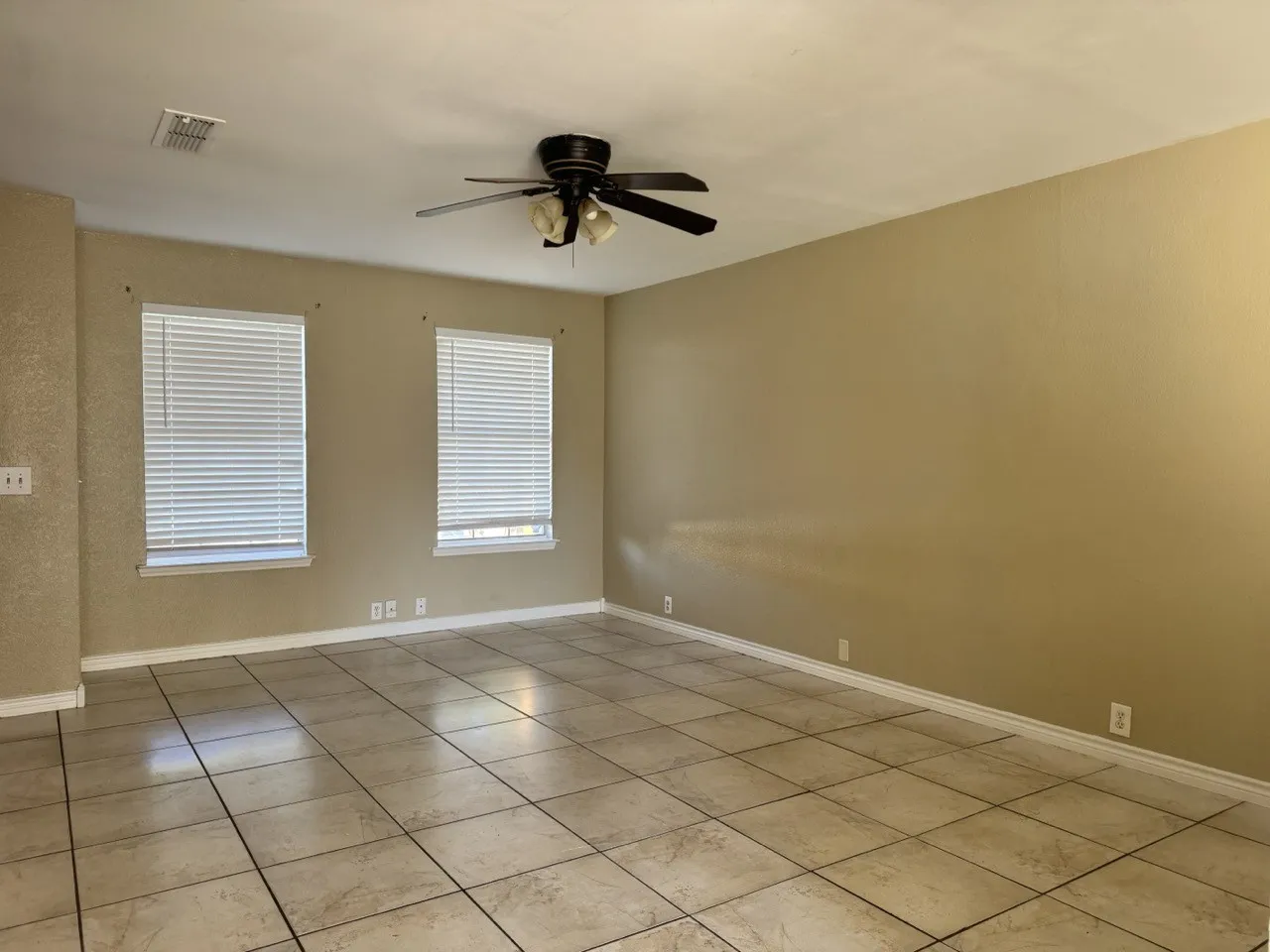 Neutral tone walls, ceramic tile flooring, two windows with blinds, and a ceiling fan with integrated lighting