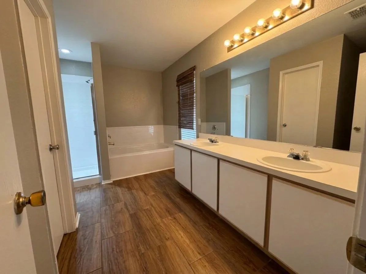 Wood-finish flooring, dual vanity with integrated sinks, large mirror, tiled shower, and a built-in bathtub