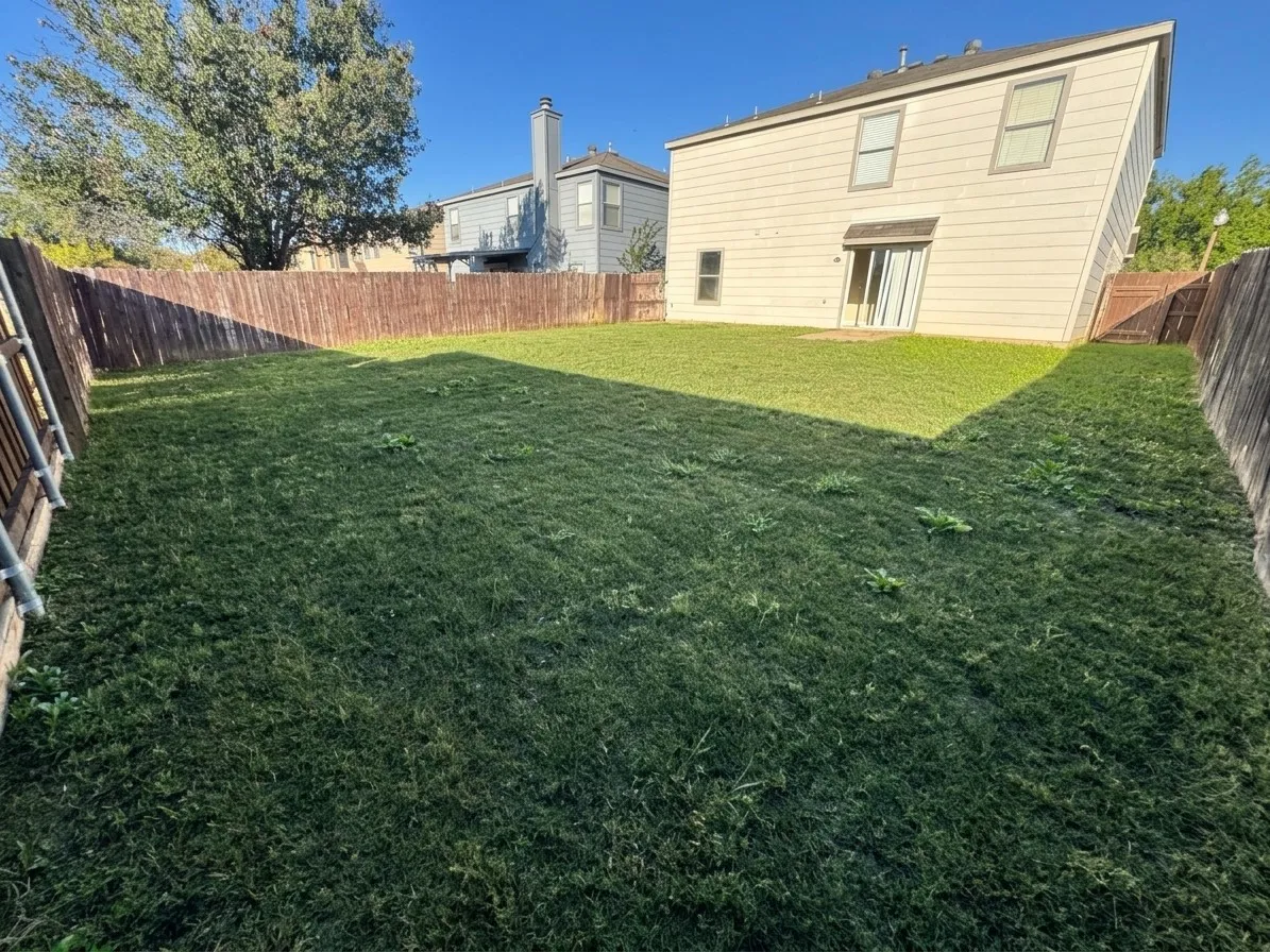 Expansive backyard with a manicured lawn, full perimeter privacy fencing, and a concrete patio