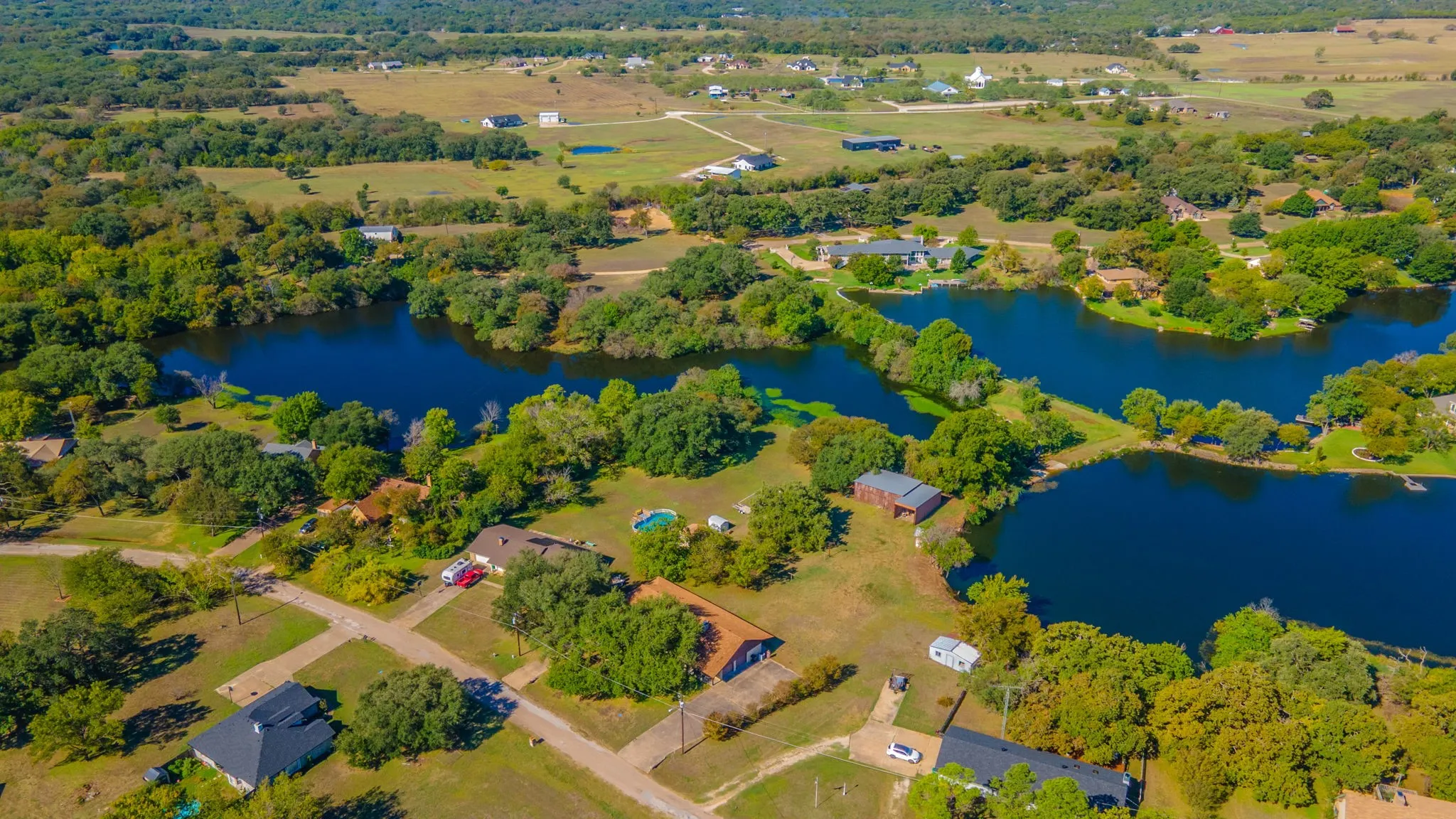 Expansive aerial landscape featuring multiple bodies of water, abundant mature trees, and surrounding residential properties