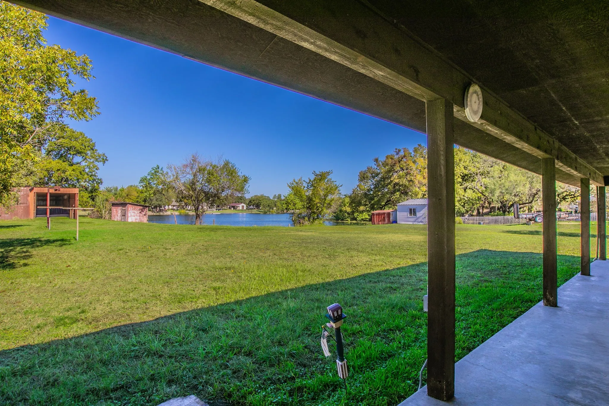 Covered concrete porch, overlooking a grassy expanse, mature trees, and  the shoreline of a small lake. Property line goes into the lake. Confirm with a survey.  Rumors have it that there are some fish in there!