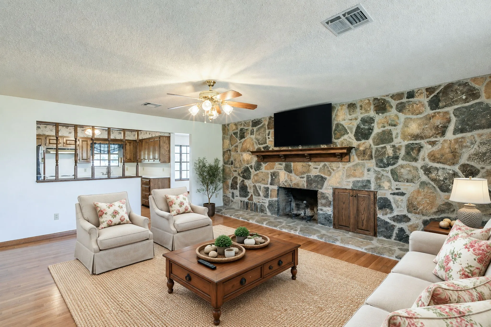 Stone-clad fireplace with wood mantle, warm wood-finish flooring, and a ceiling fan with integrated​​‌​​​​‌​​‌‌​‌‌​​​‌‌​‌​‌​‌​​​‌​​ lighting