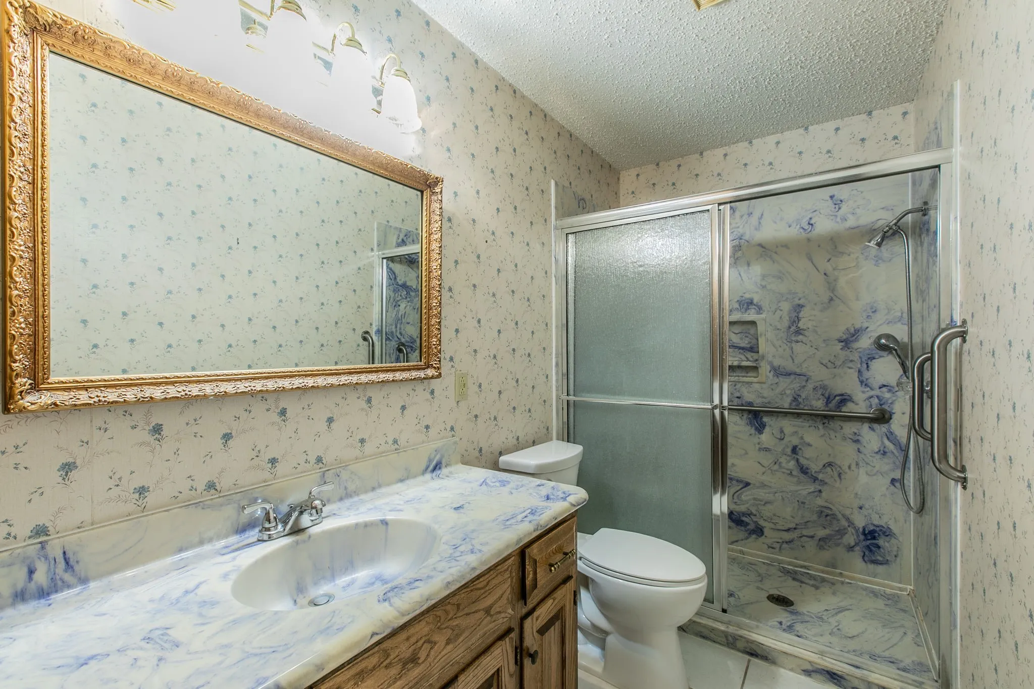 Vanity with an integrated sink and blue-swirl countertop, wood-finish cabinetry, and an ornate framed mirror