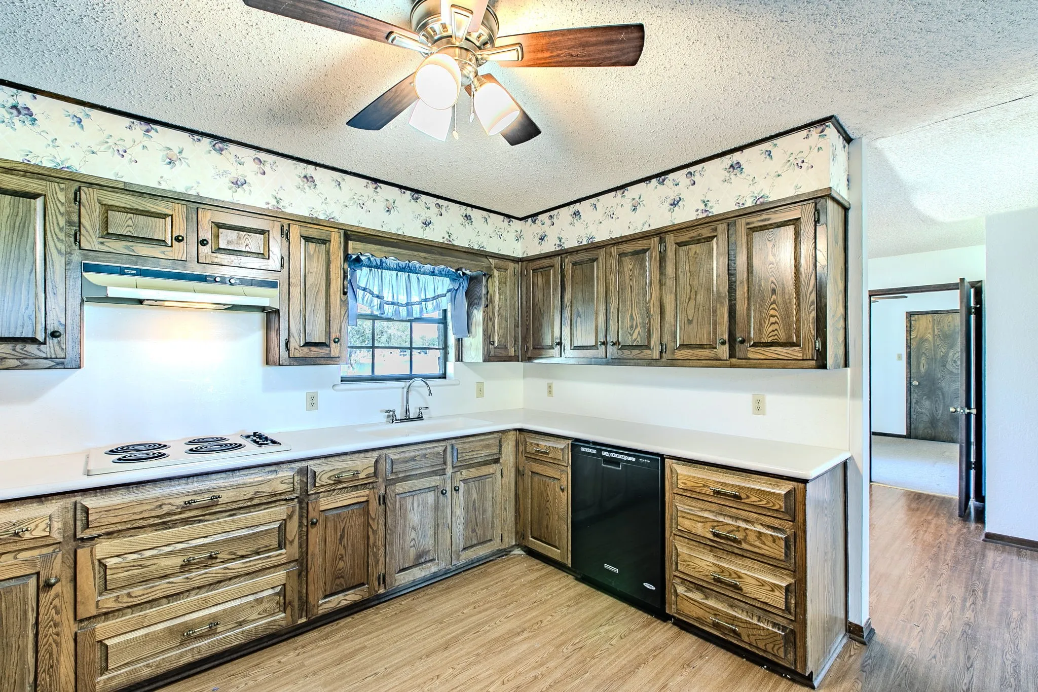 Kitchen with wood-finish cabinetry, white countertops, built-in stovetop, and overhead ventilation