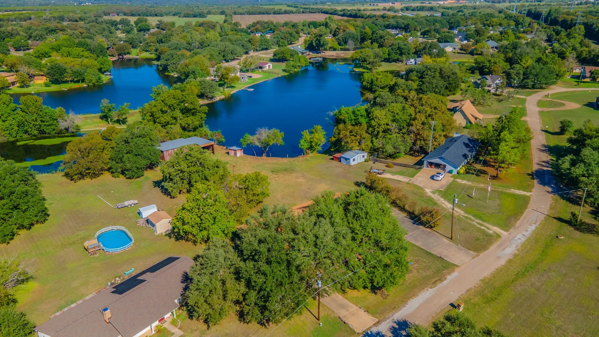 Expansive property featuring multiple structures, mature trees, a residence with an attached garage, and bordered by 2 bodies of water.