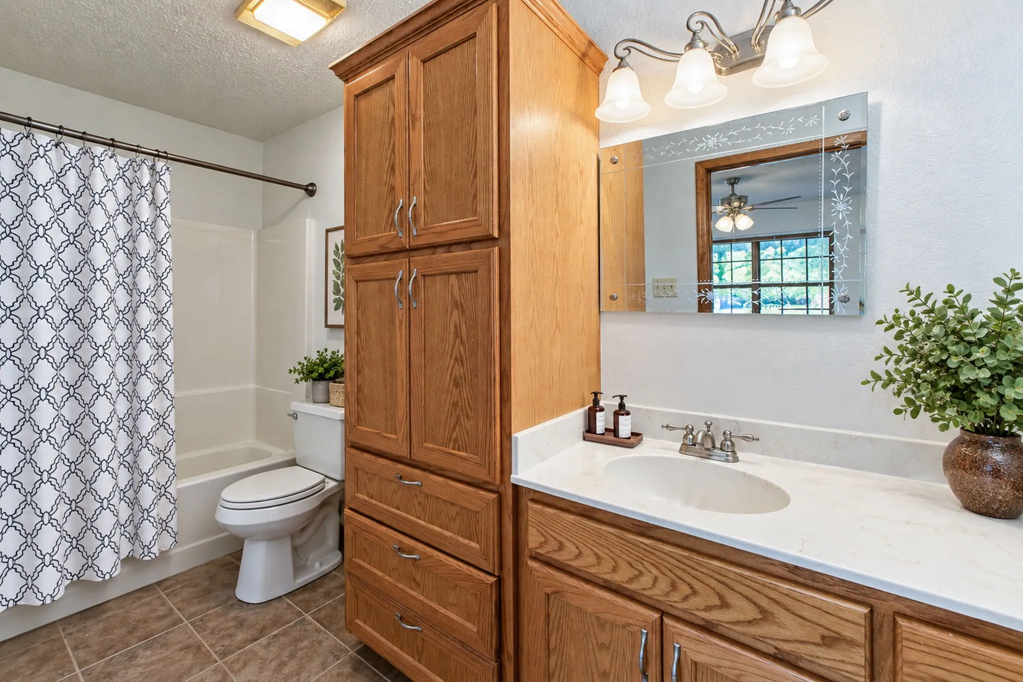 Bathroom featuring a single vanity with an integrated sink, a built-in wood-finish storage cabinet, a tub with a shower, and tiled flooring