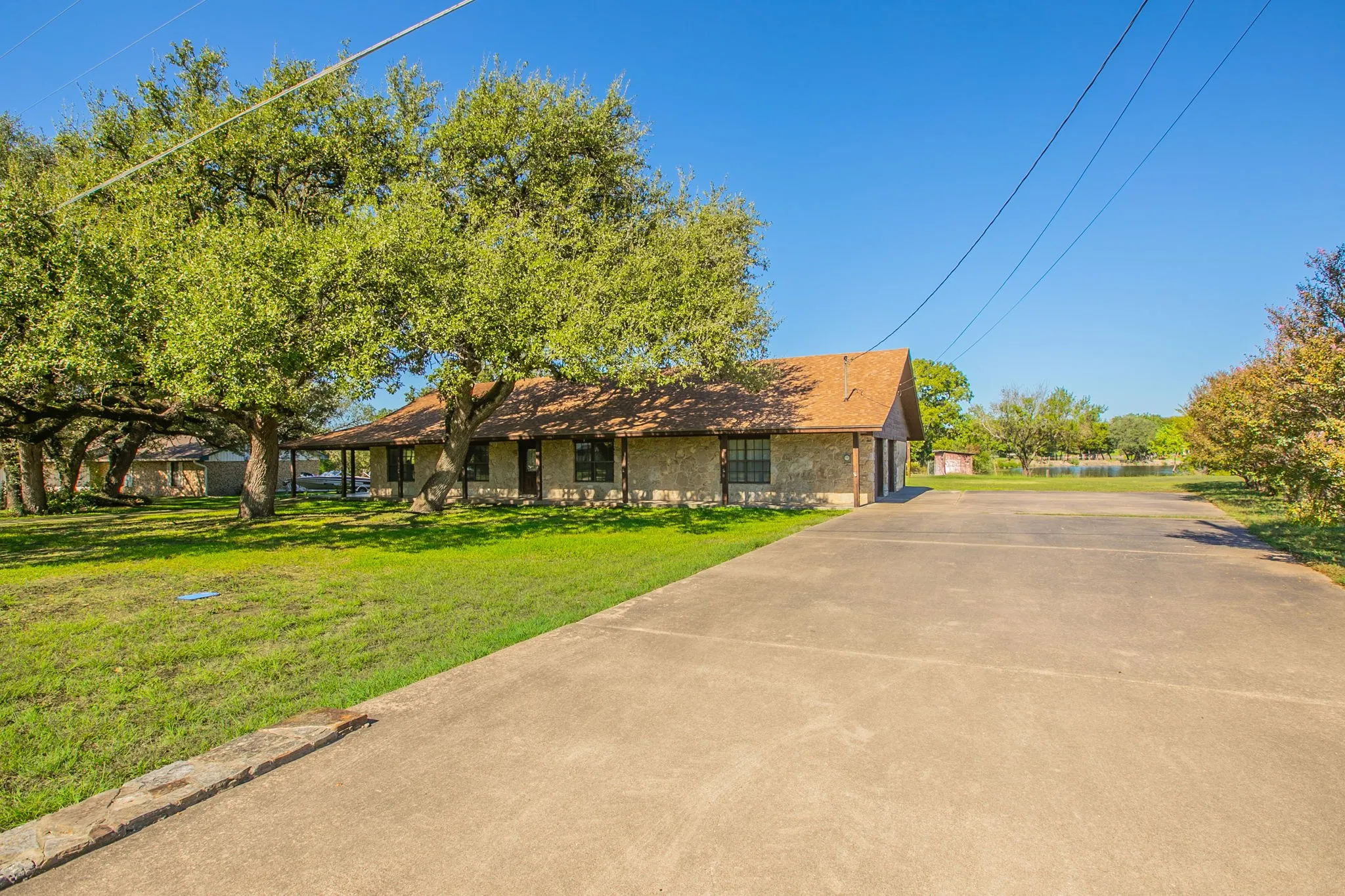 Stone exterior residence with a covered front porch, concrete driveway leading to a 2 car side garage and mature trees