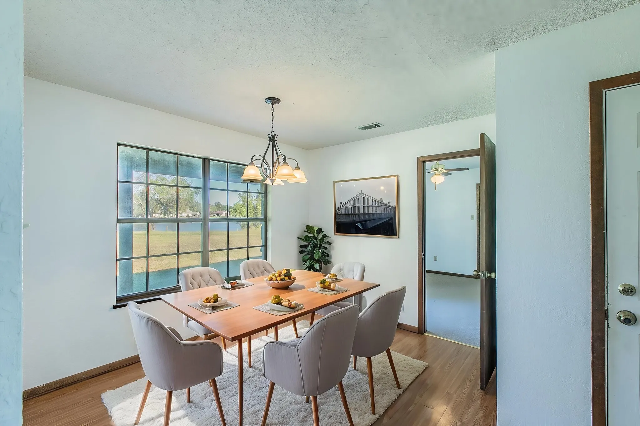 Large grid-pattern window, wood-finish laminate flooring, and a multi-bulb chandelier