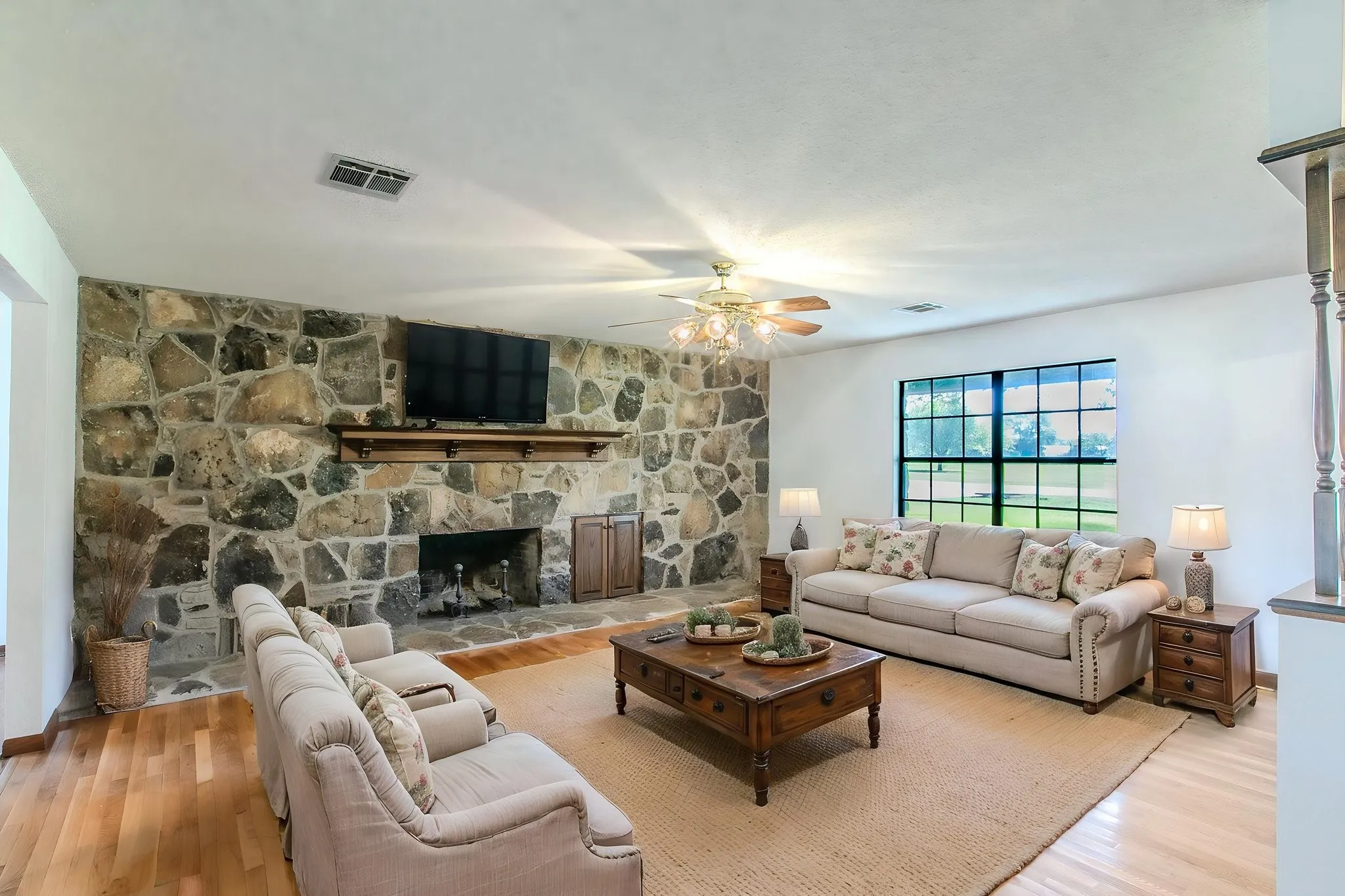 Stone-faced fireplace with a wood mantle, wood-finish flooring, and a ceiling fan