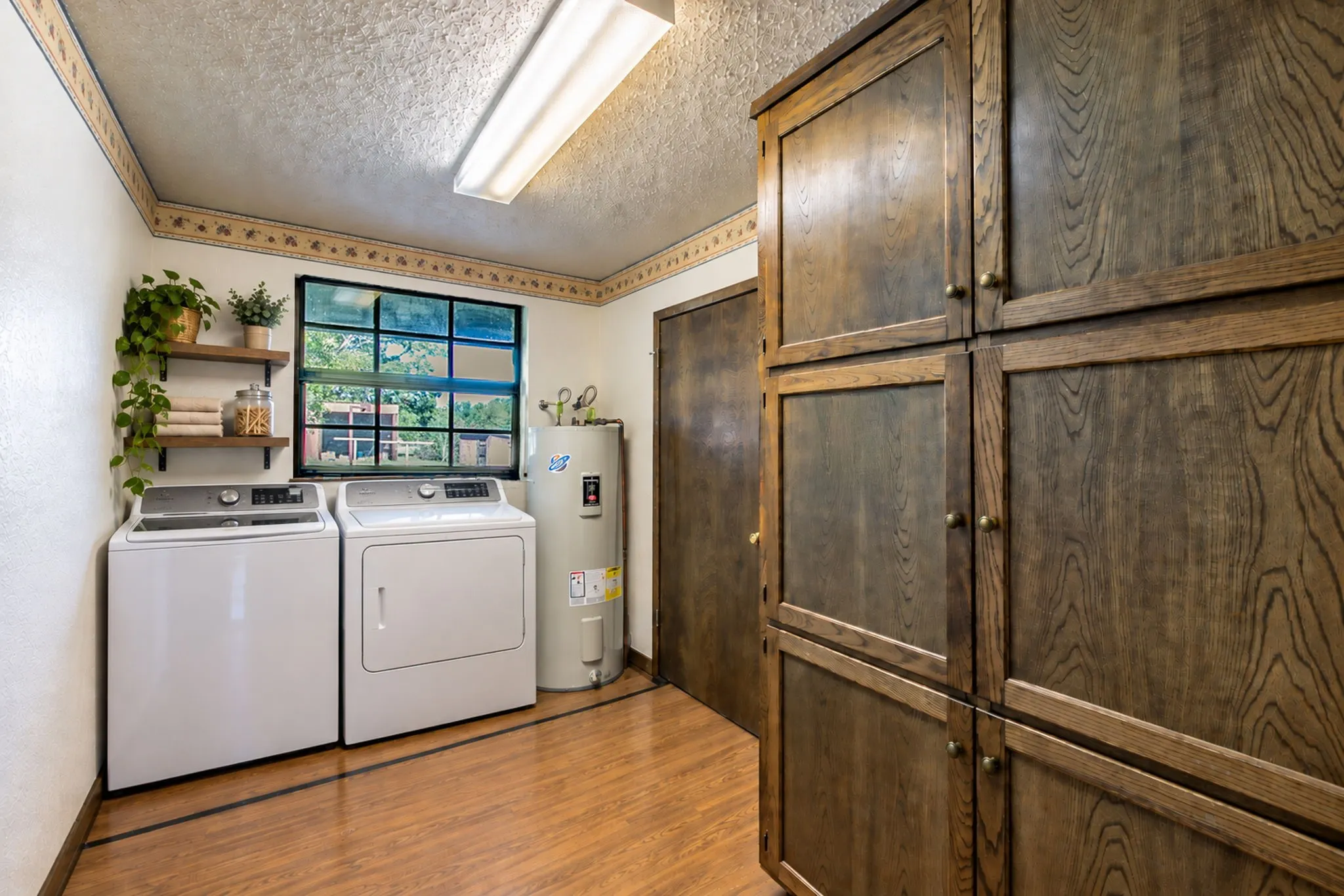 Wood-finish flooring, built-in storage cabinetry, two floating wood shelves, and a water heater