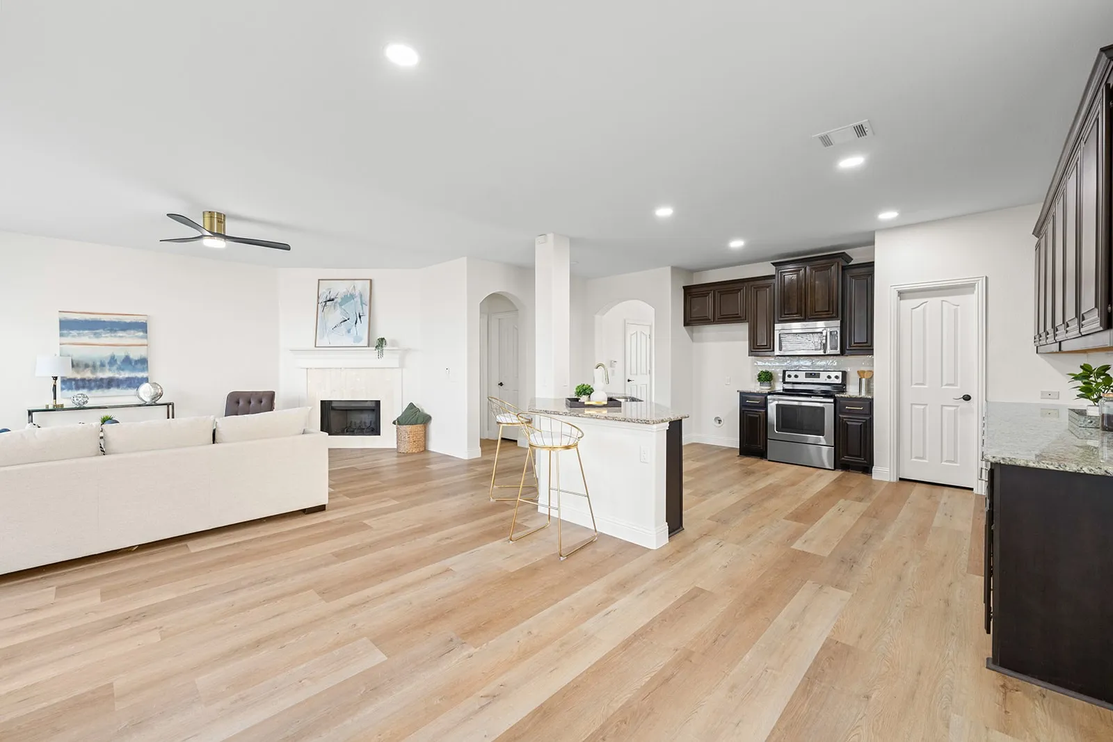 Open-concept living space featuring wood-finish flooring, a fireplace with a white mantel, recessed lighting, and a ceiling fan