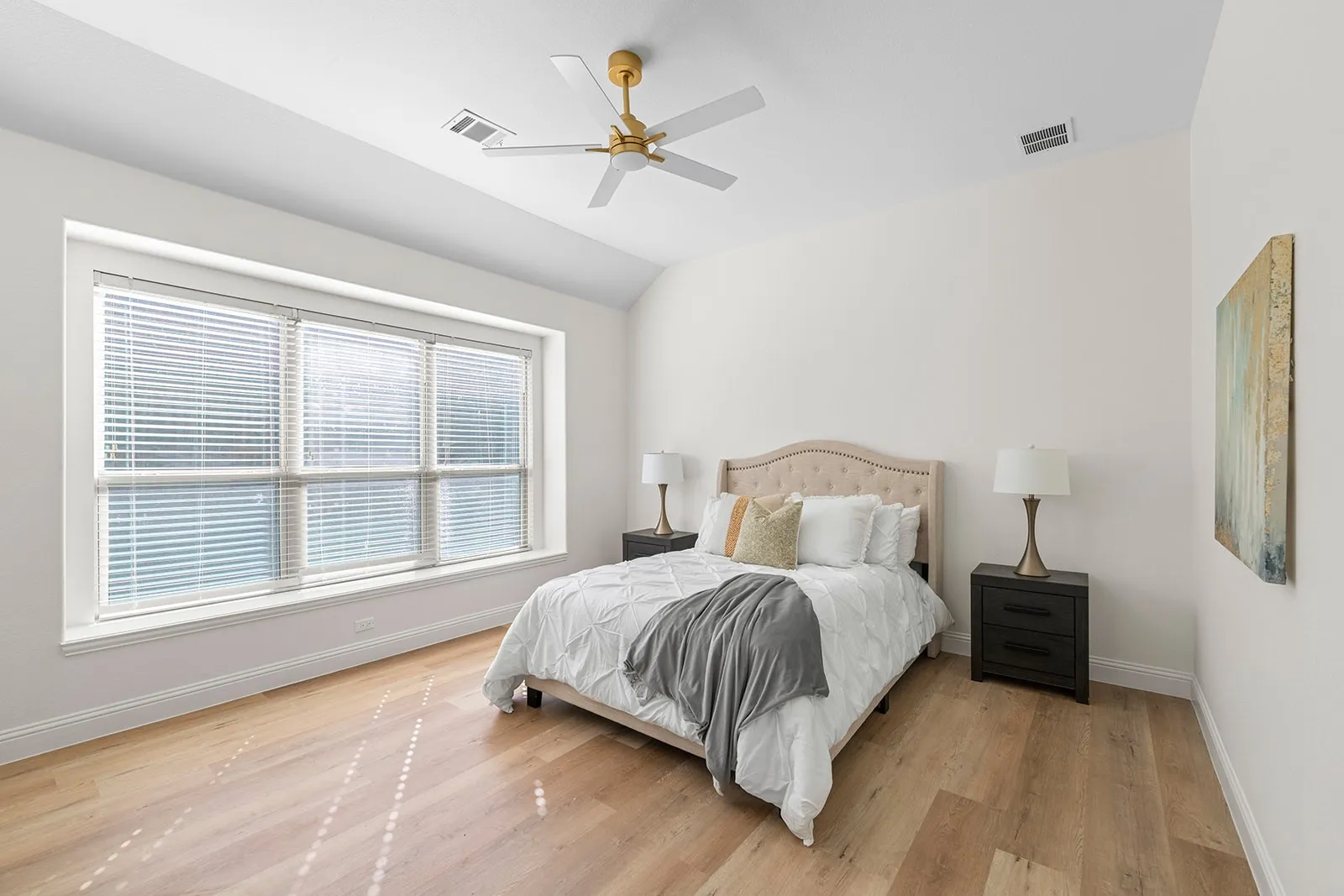 Vaulted ceiling with a gold-tone ceiling fan, light wood-finish flooring, and a wide window with blinds