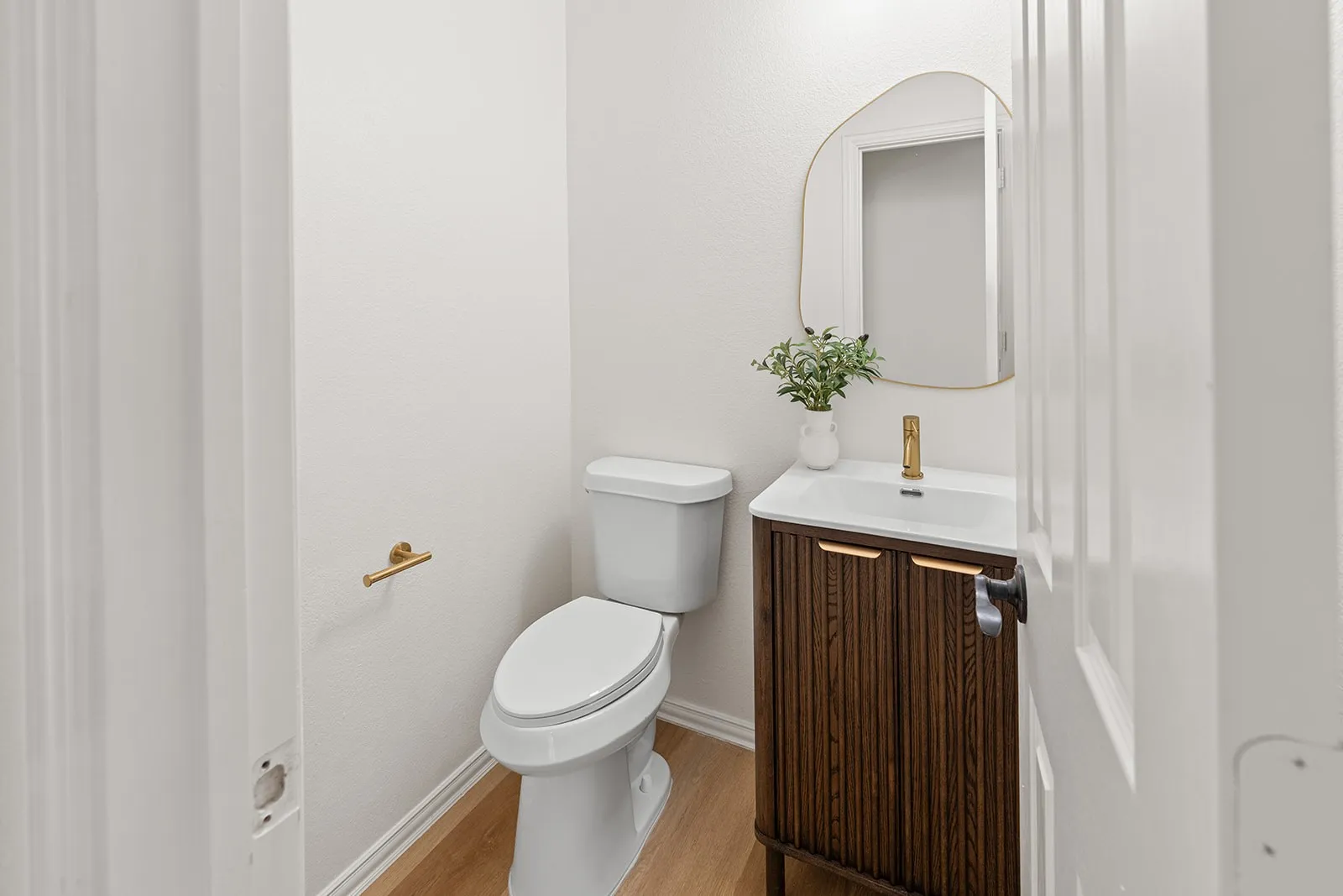 White vanity with wood-finish fluted cabinetry, integrated rectangular sink, gold-finish faucet, and coordinating gold-finish mirror