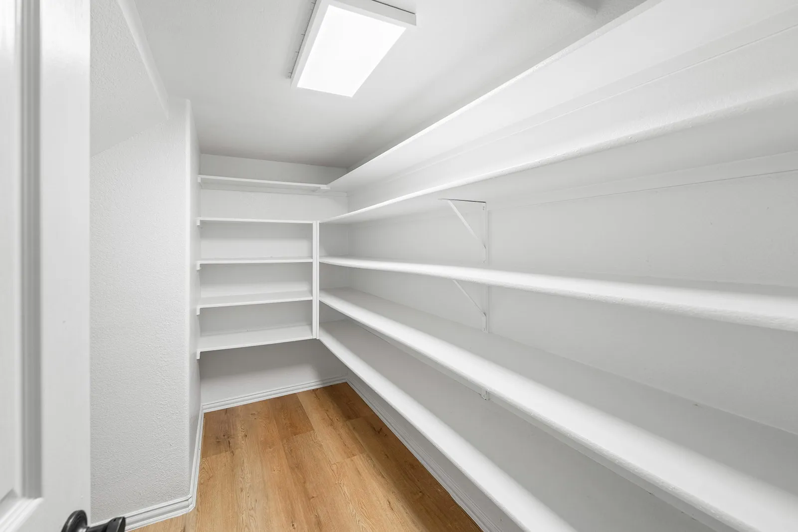 White built-in shelving, wood-finish flooring, recessed ceiling light