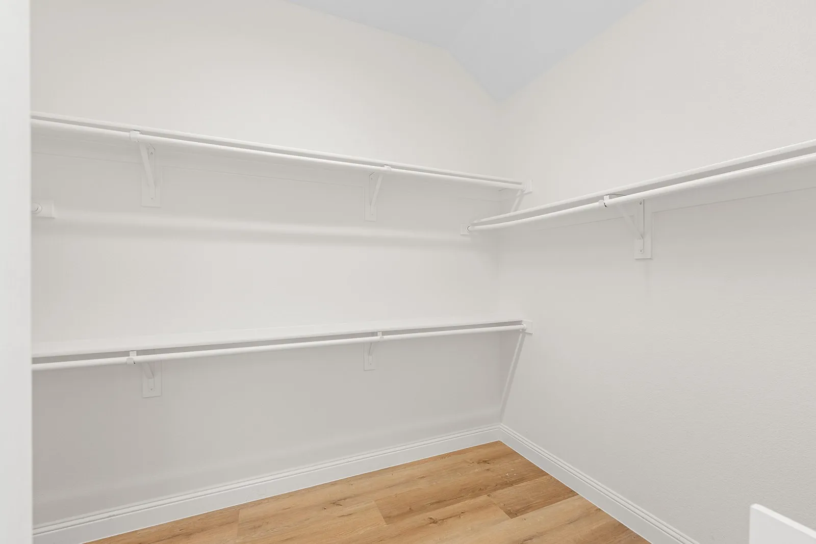 Walk-in closet with multiple white wire shelving units and wood-finish flooring