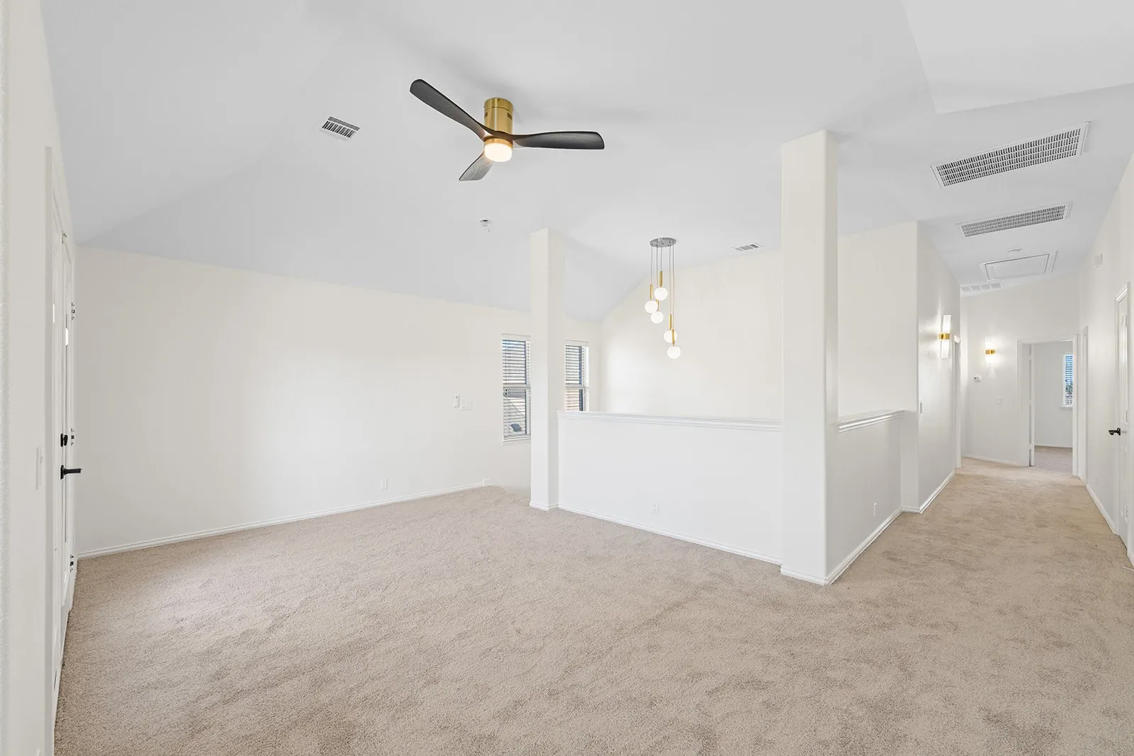 Spacious carpeted room featuring a vaulted ceiling with a modern ceiling fan, a window, and a built-in wall niche, alongside a hallway with wall sconces and a multi-pendant light fixture