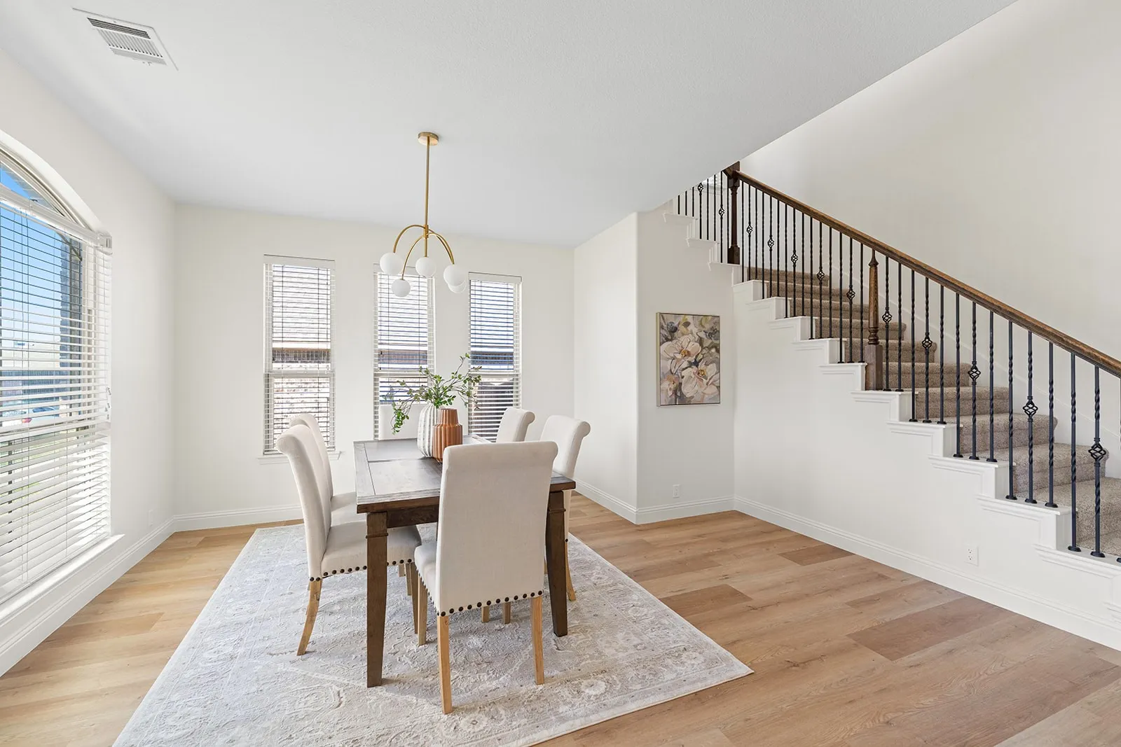 Wood-finish flooring, multiple windows, arch-top window, iron baluster staircase, and a contemporary chandelier