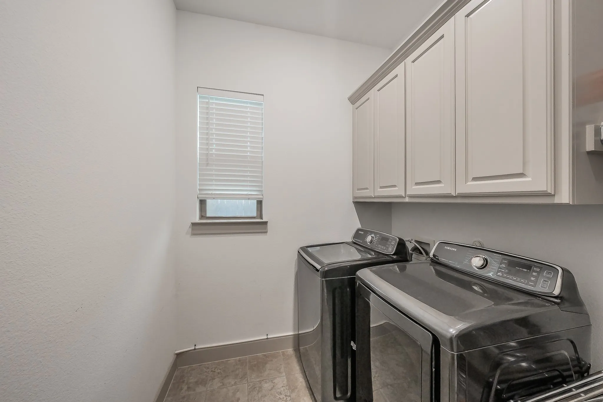 Dedicated spacious laundry room featuring built-in cabinetry and a high-set window for natural light and ventilation