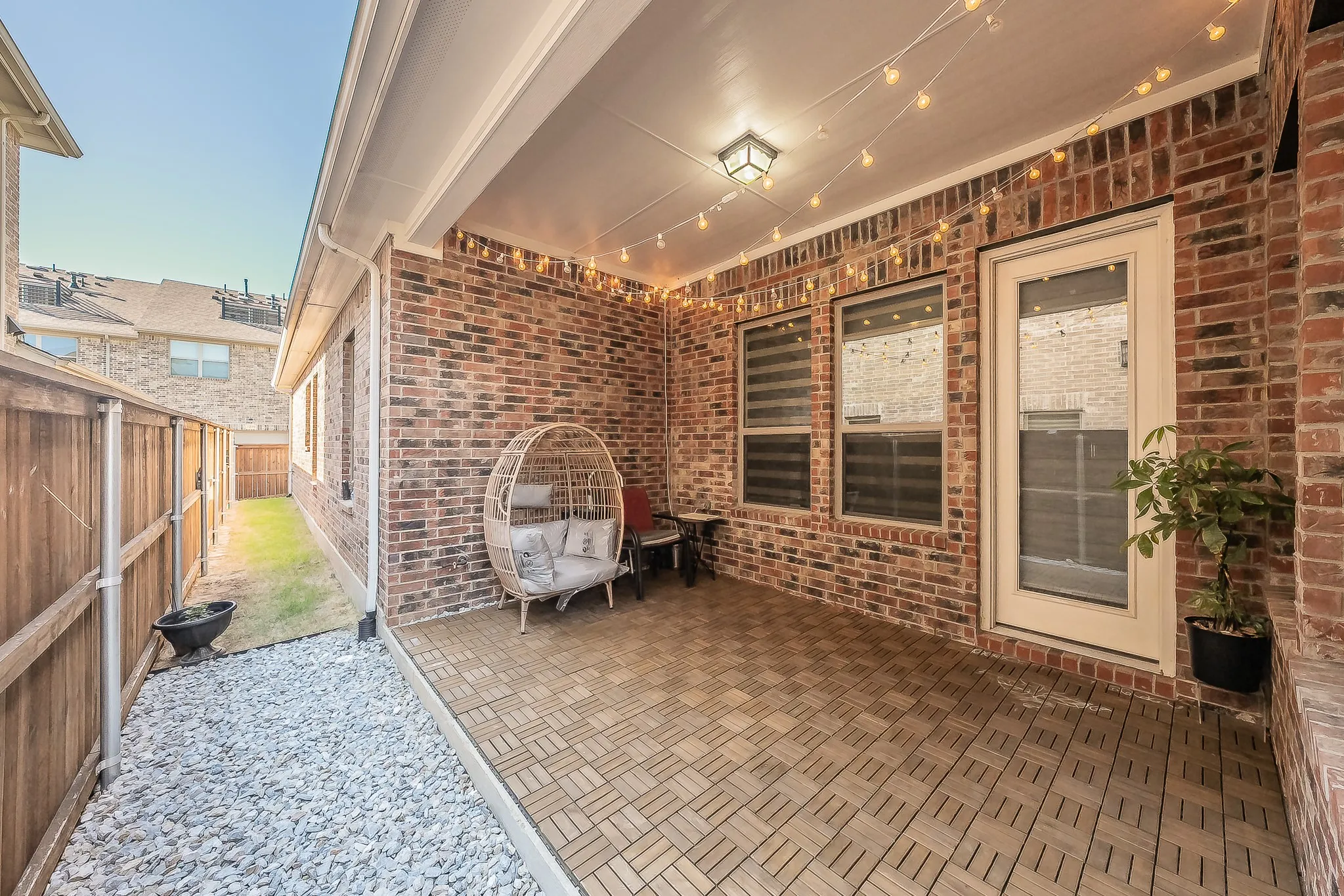 Covered patio with brick exterior, wood-finish tile flooring, recessed lighting, and direct outdoor access off the kitchen, perfect for grilling