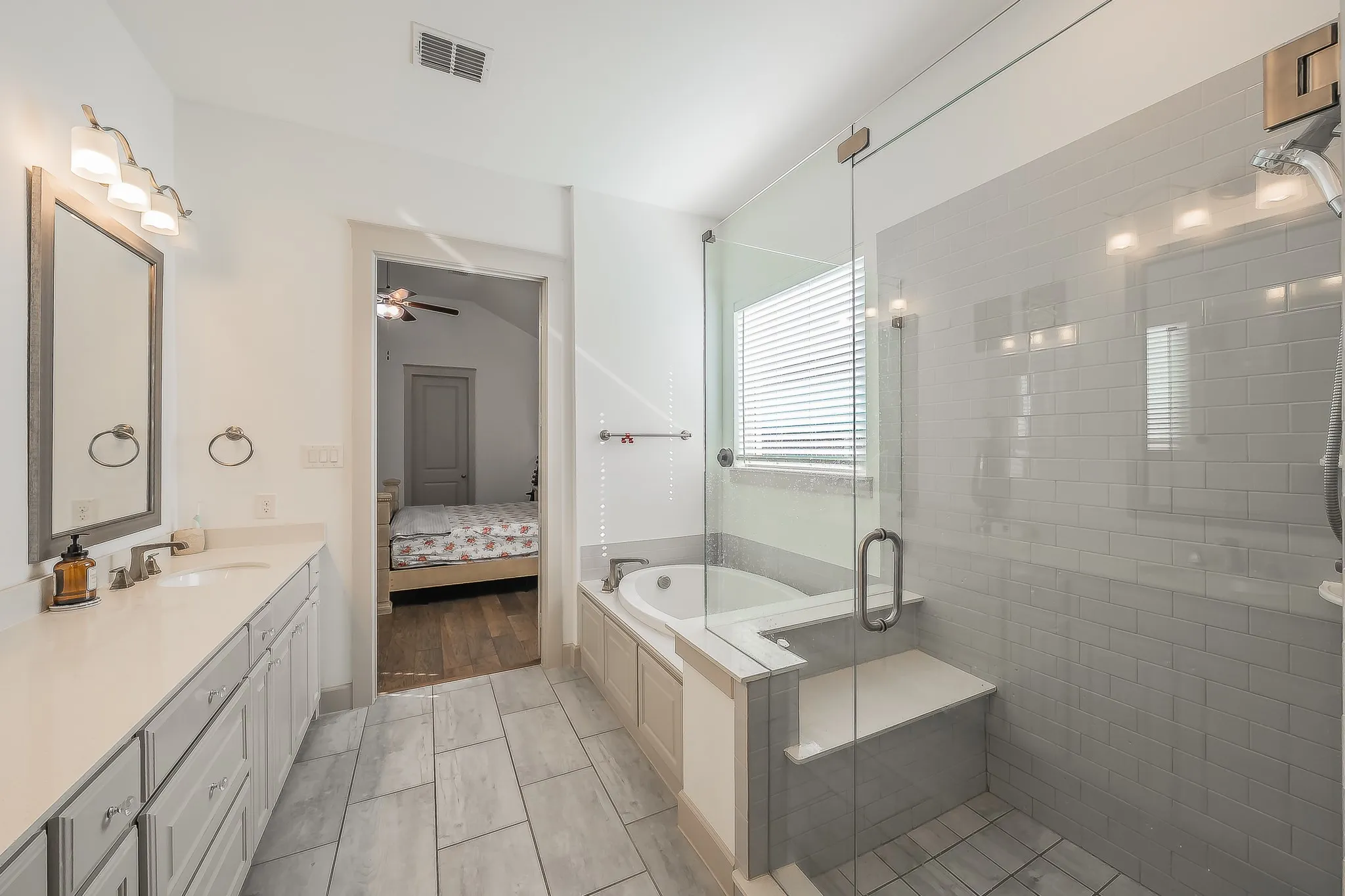 Spacious bathroom with a walk-in shower featuring a bench and glass enclosure, a built-in bathtub, a double vanity with an undermount sink, and tile flooring