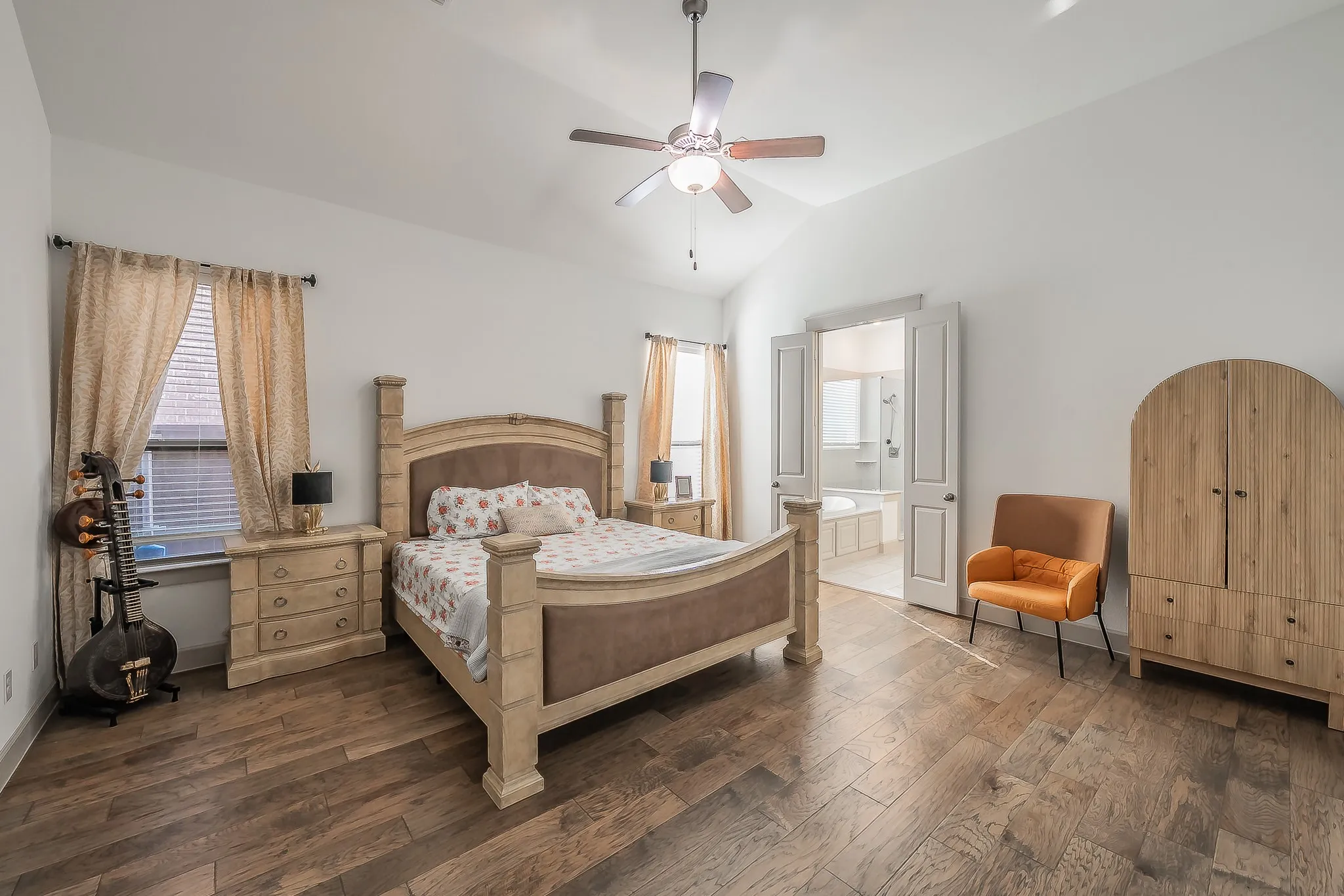Vaulted ceiling with a ceiling fan, wood flooring, and double doors opening to an ensuite bathroom with a tub, separate shower, two sinks and a second closet
