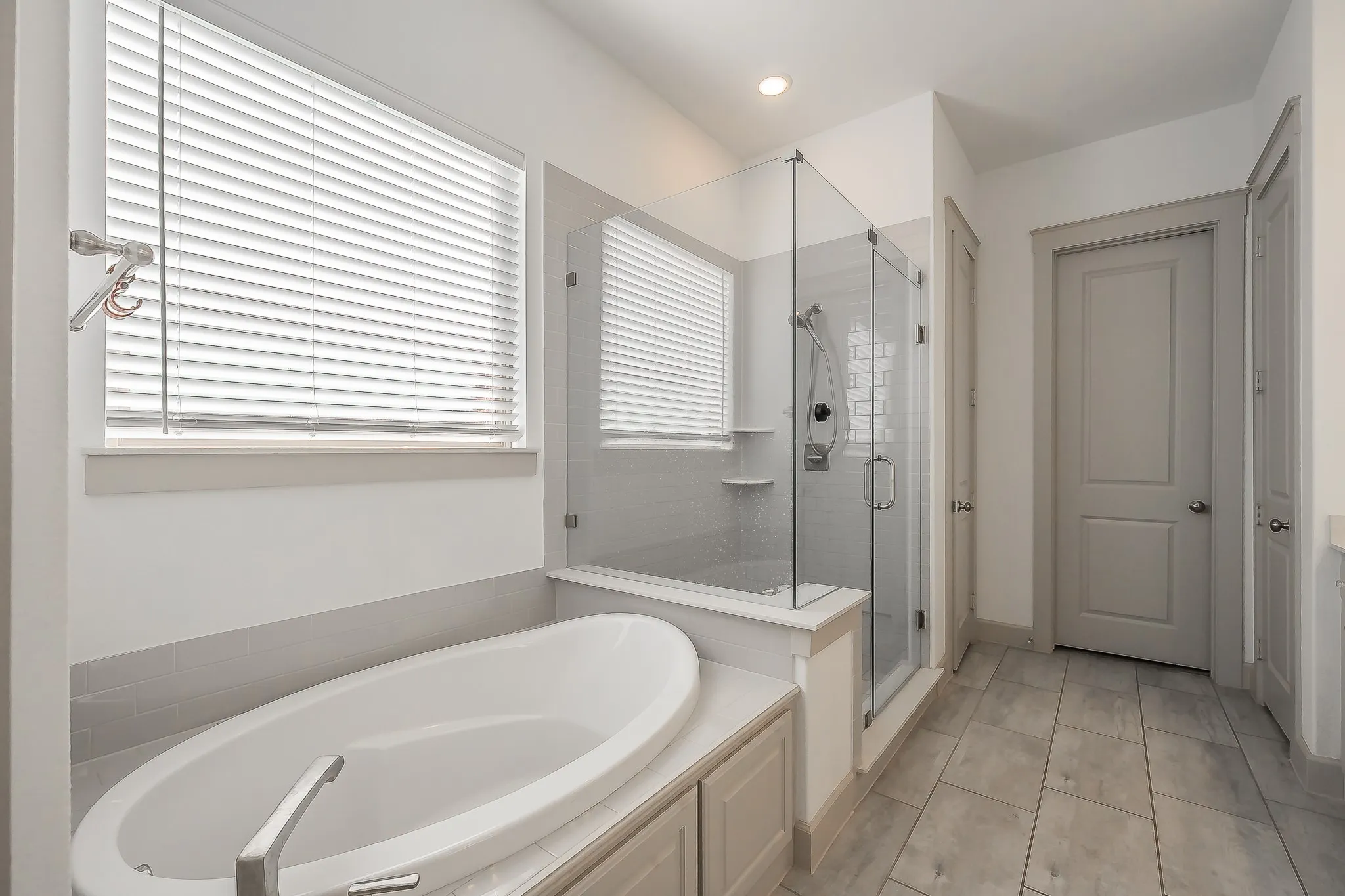 Freestanding oval soaking tub, glass-enclosed shower with subway tile, tiled flooring, a bench and plenty of natural light