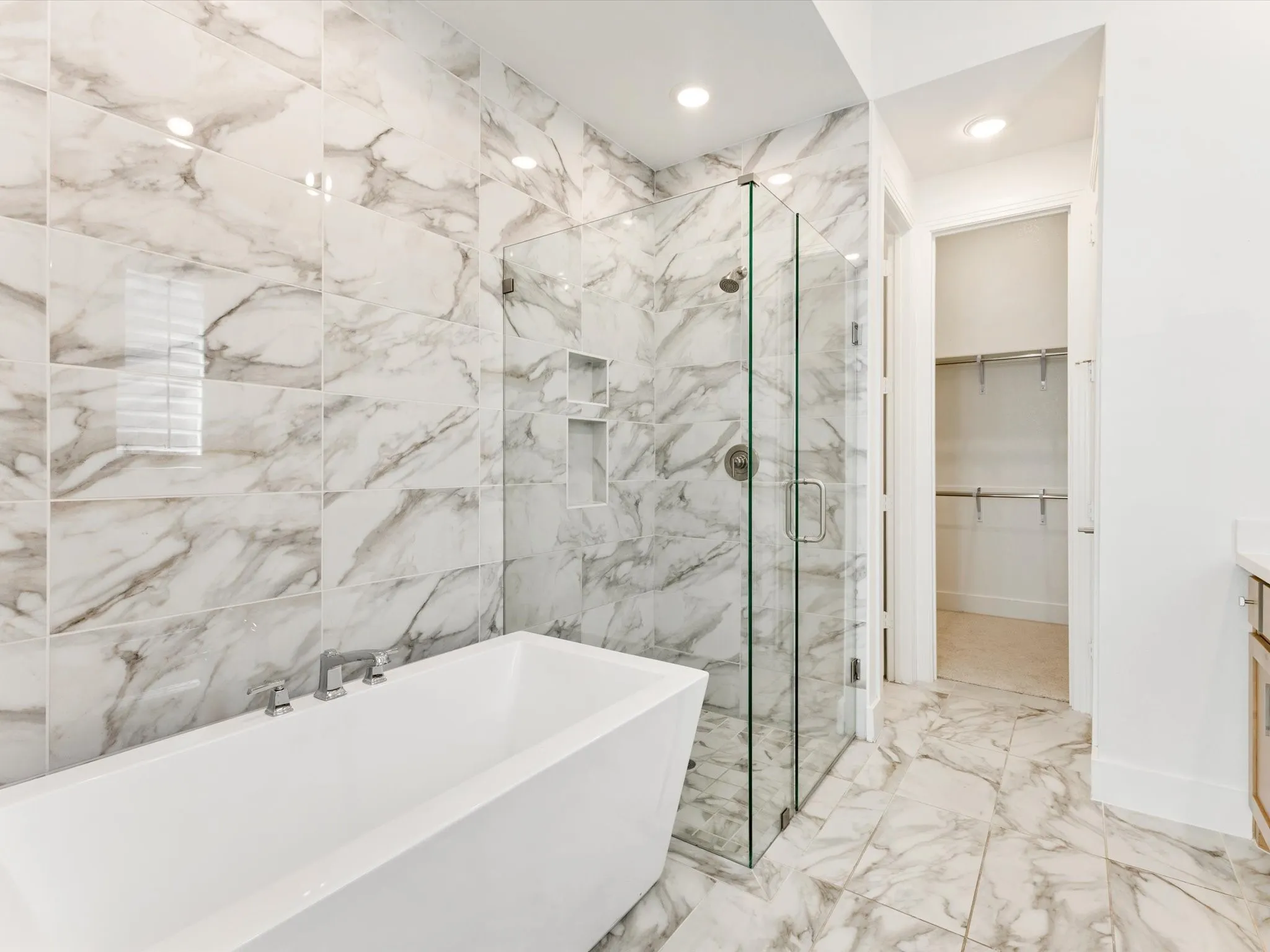 Freestanding soaking tub with chrome fixtures, large format tile flooring, and a glass-enclosed shower with integrated shelving