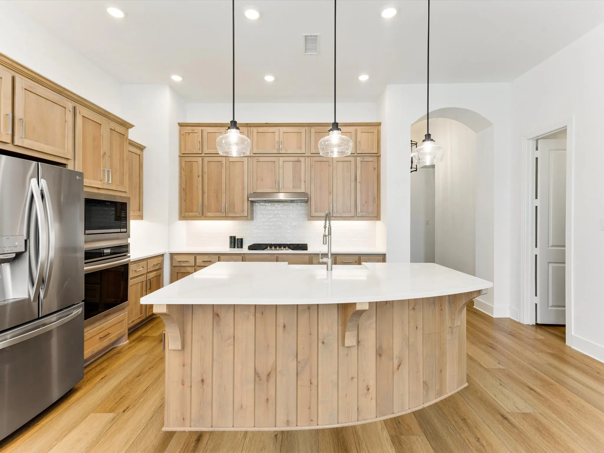 Kitchen featuring a curved island with a white countertop, light wood cabinetry, stainless steel appliances, and wood-finish flooring