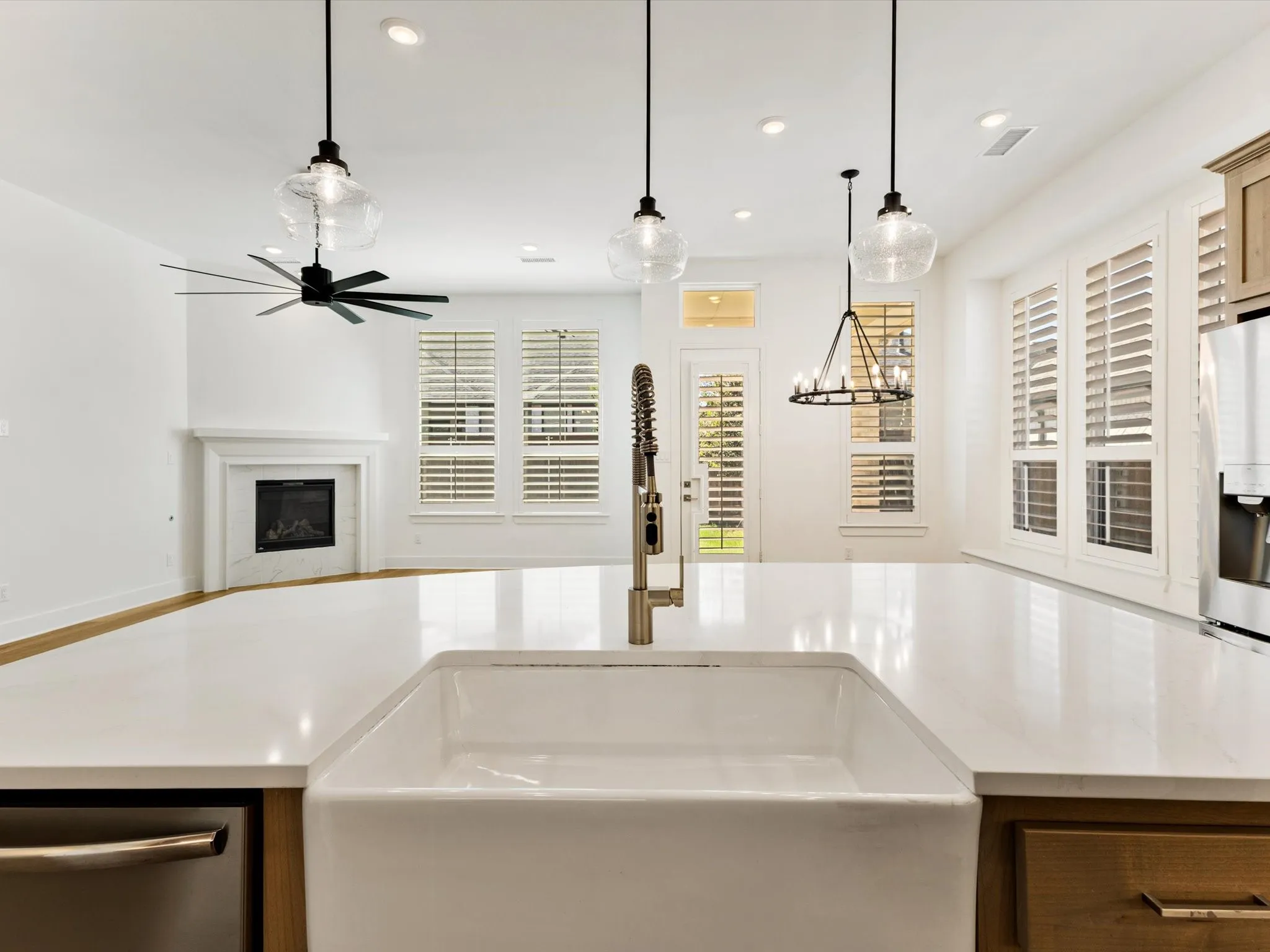 White farmhouse sink with a gold-tone pull-down faucet, white countertops, and recessed lighting