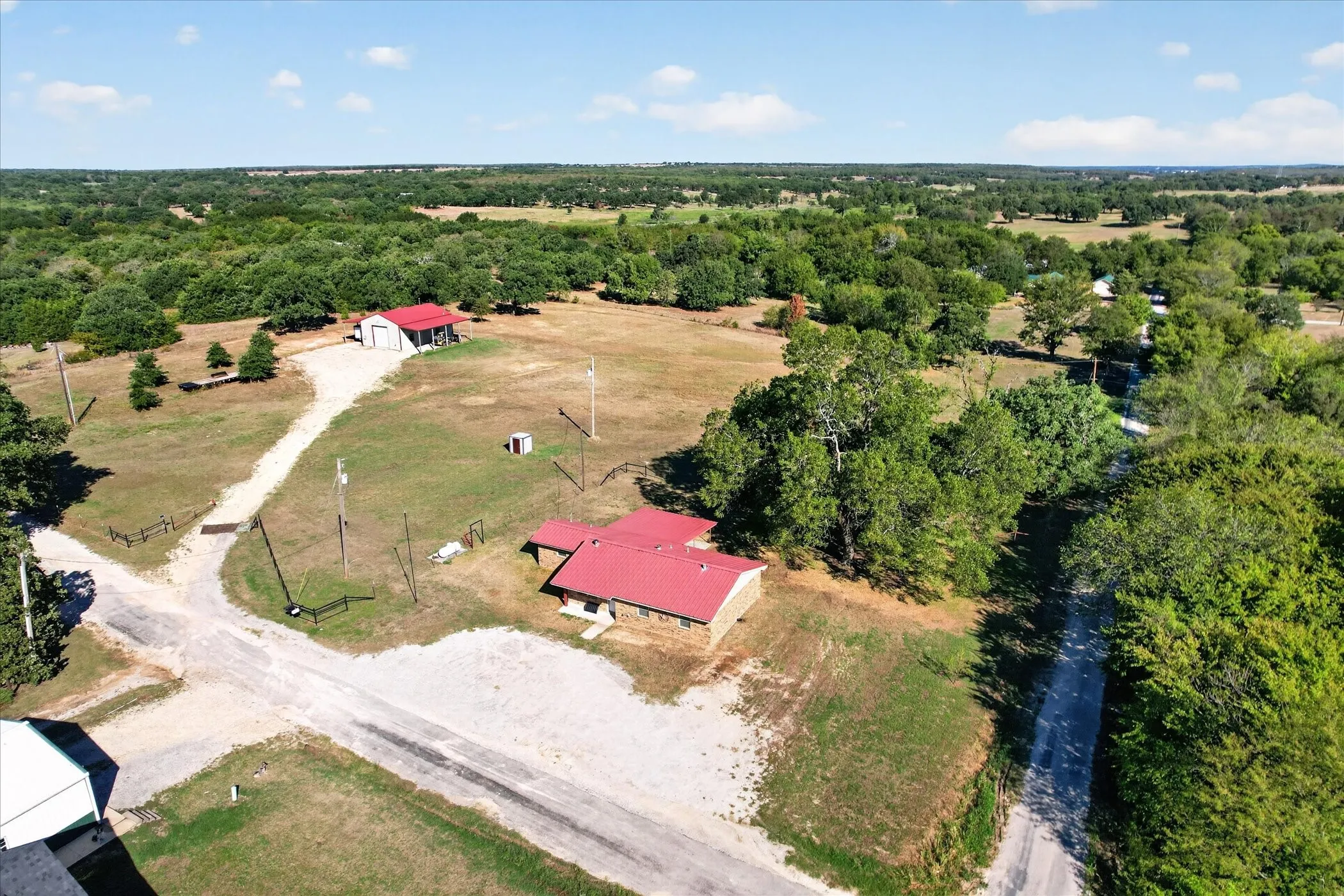 Expansive property featuring a main structure with a red metal roof, a secondary detached building, and a private gravel driveway