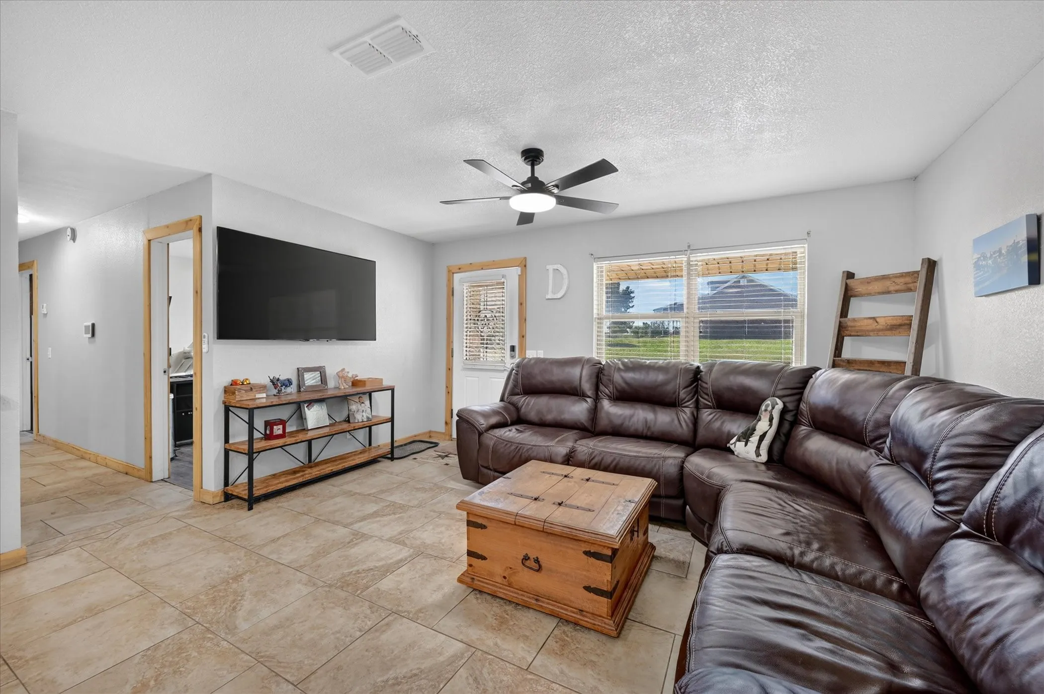 Tiled flooring, ceiling fan, white interior walls, wood-trimmed doorways, and a window with blinds