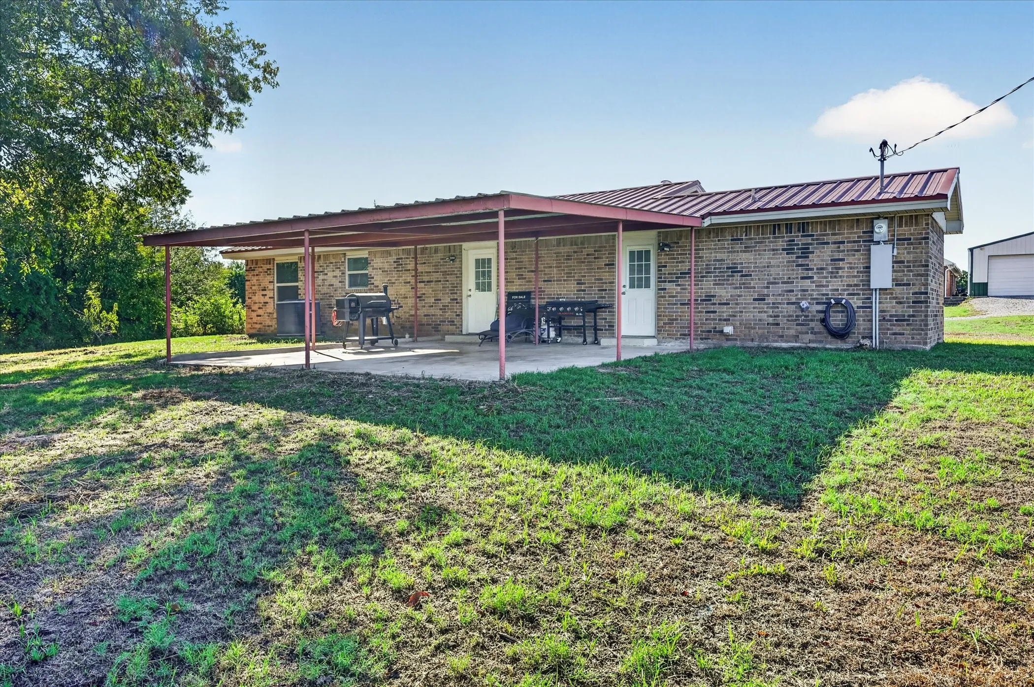 Brick exterior with a metal roof, featuring a covered concrete patio and a grassy yard