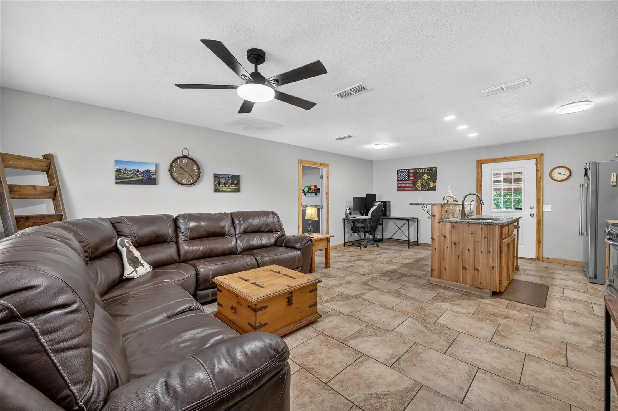 Recessed lighting, ceiling fan, tile flooring, wood-finish trim, and a kitchen island with a sink and granite countertop