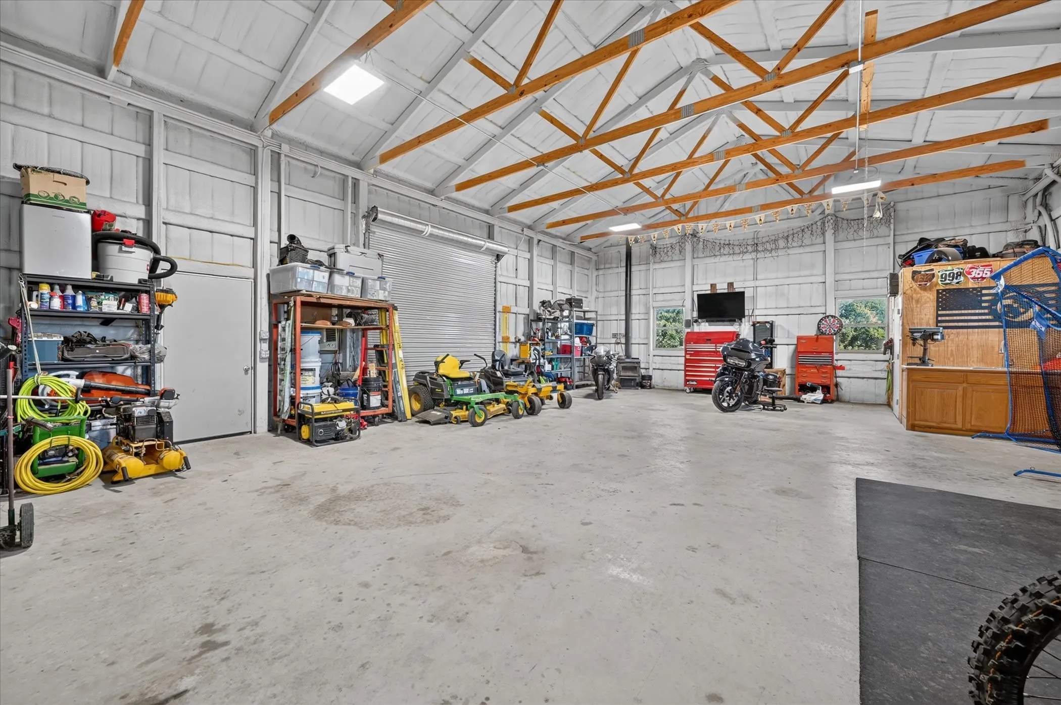Spacious outbuilding featuring exposed wood rafters, concrete flooring, skylights, and multiple roll-up garage doors