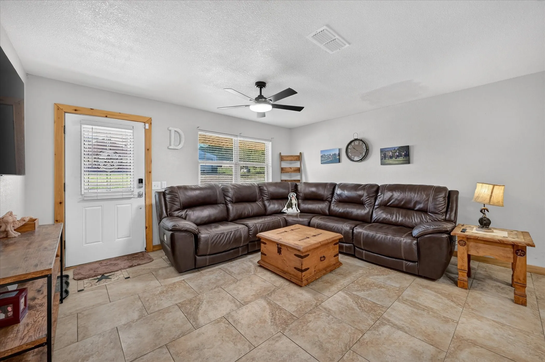 Spacious living area featuring tile flooring, a ceiling fan, and multiple windows with blinds