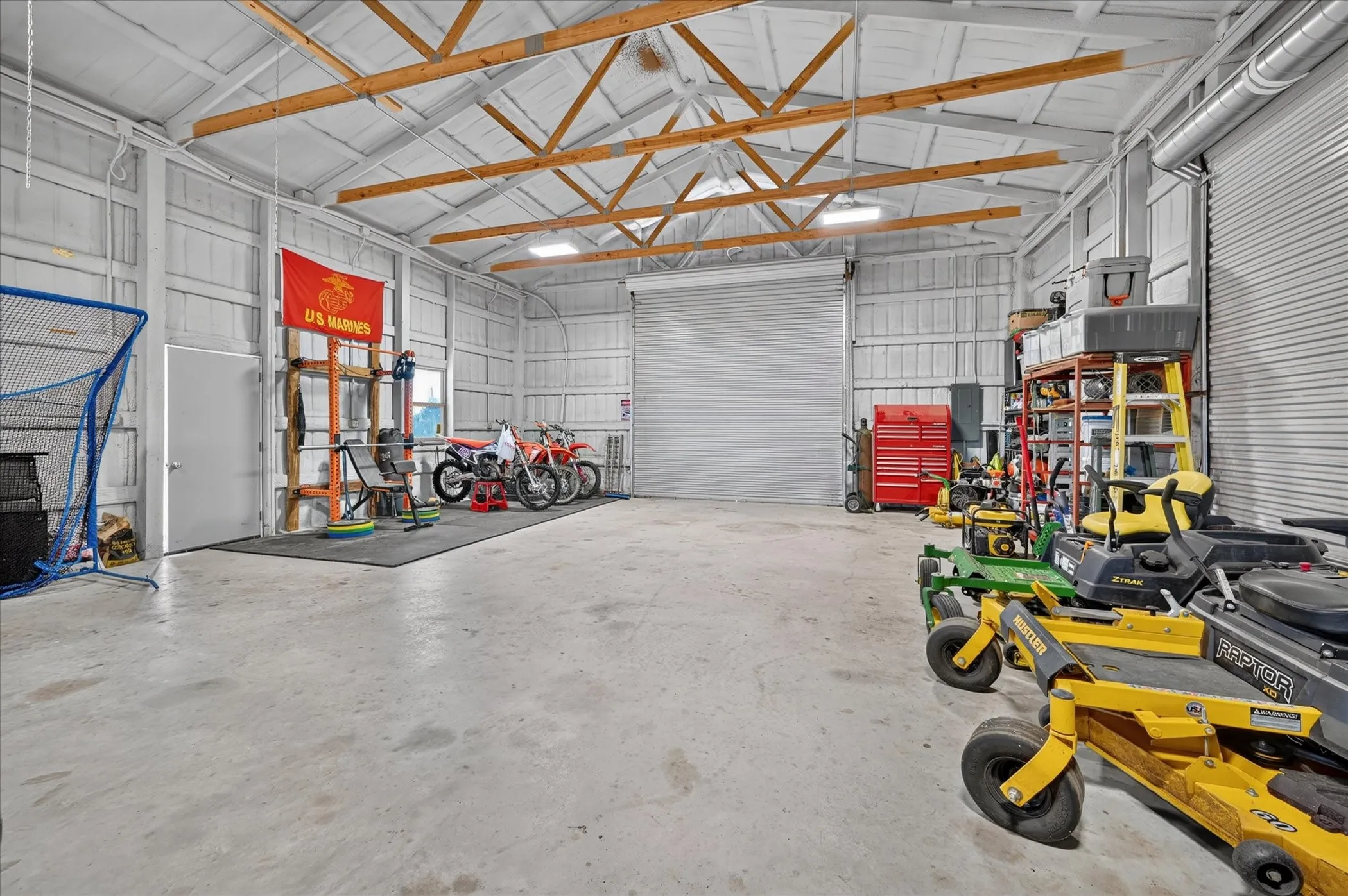 Spacious garage with exposed beam ceiling, concrete flooring, and two large roll-up doors