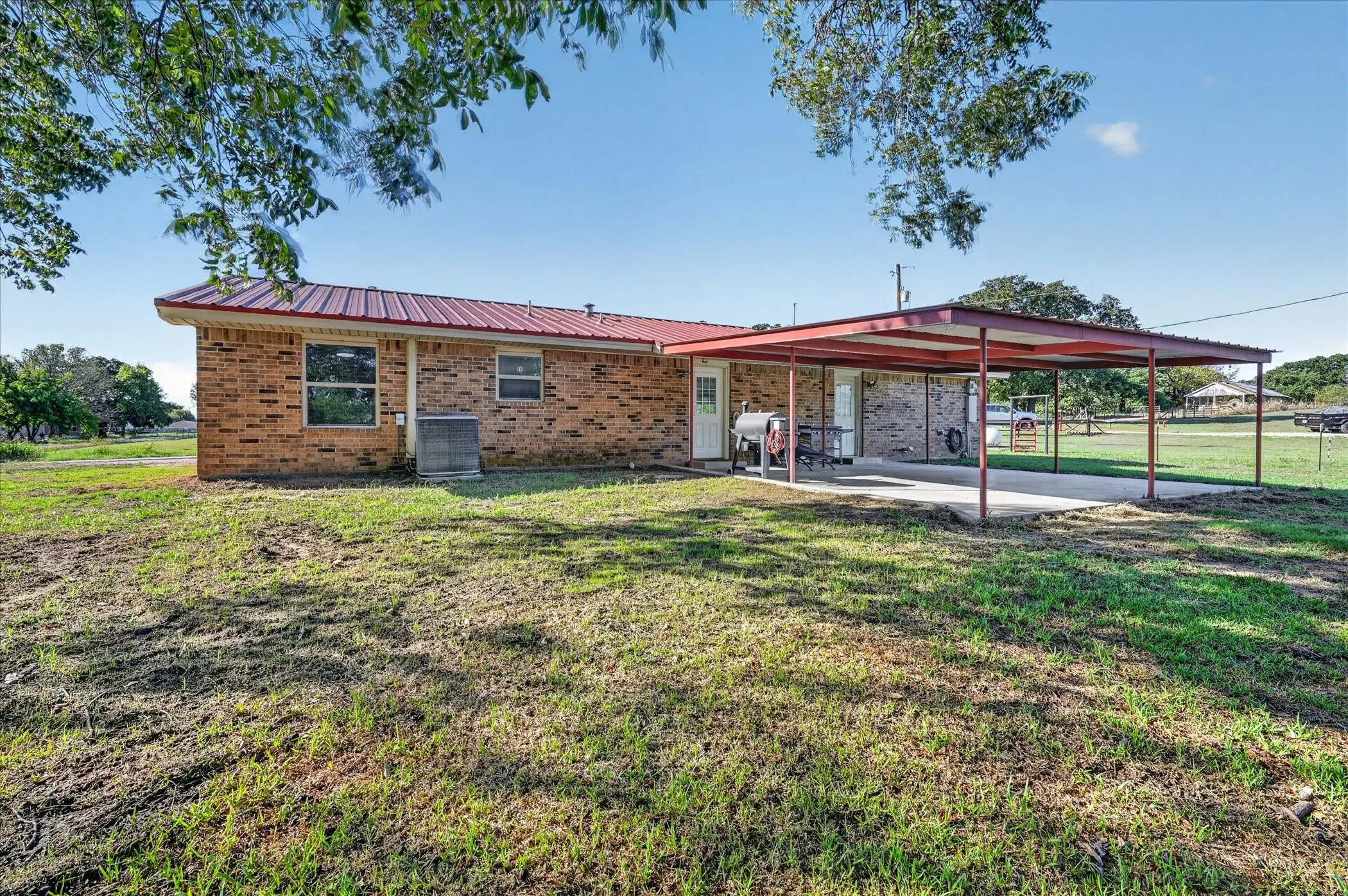 Brick exterior with a red metal roof, covered patio, and attached carport