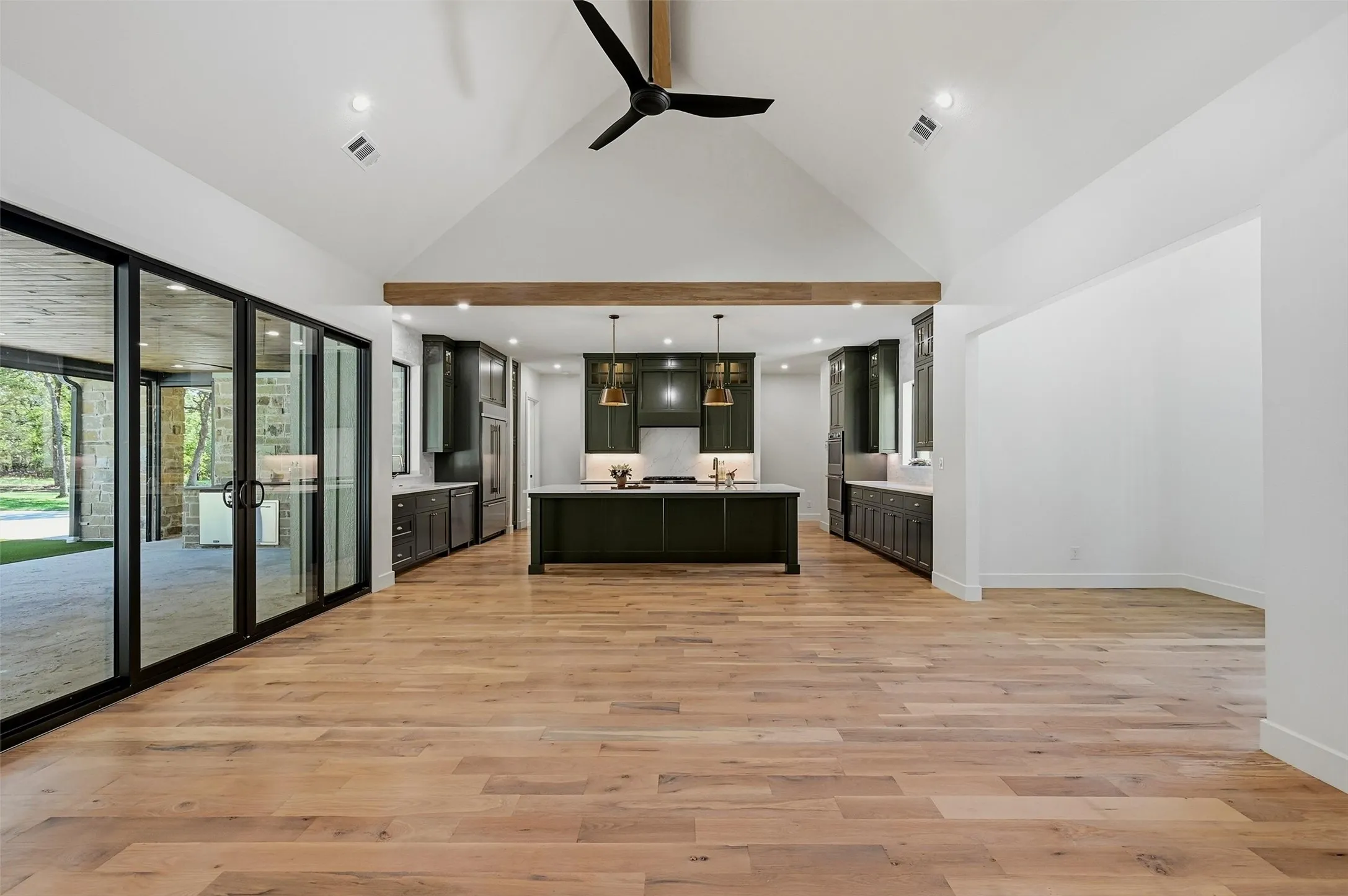 Vaulted ceiling with exposed beam, wood-finish flooring, sliding glass doors, custom inset cabinetry, and a kitchen island with pendant lighting