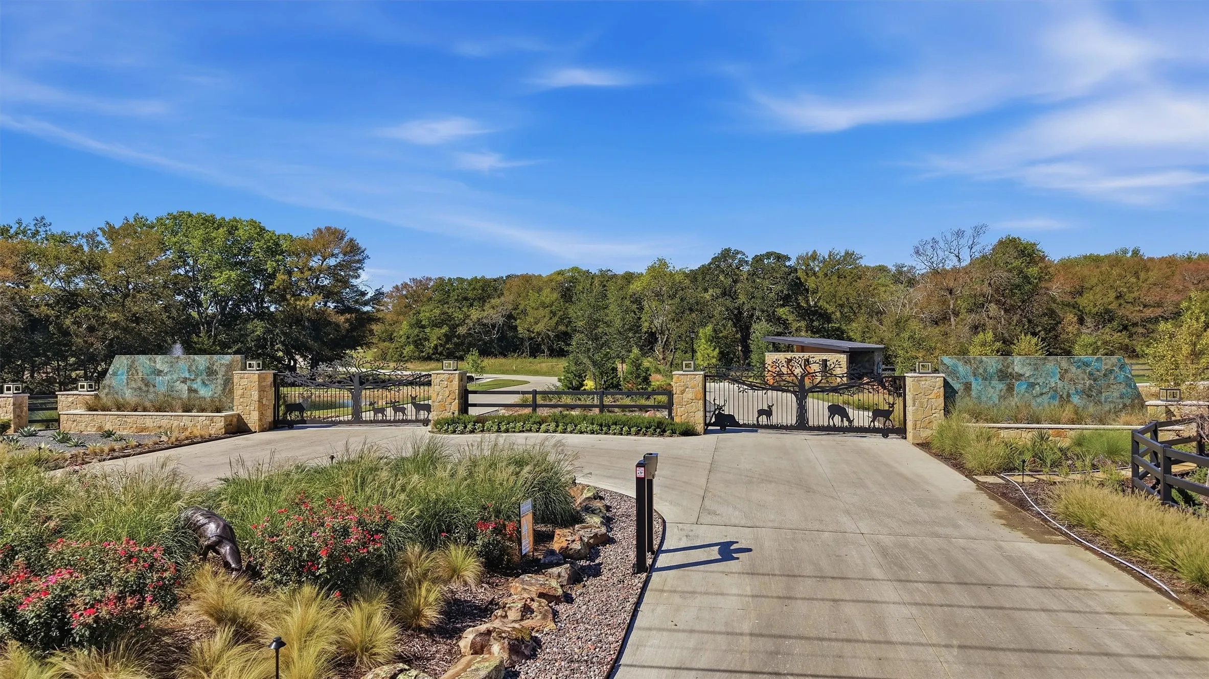 Stone pillar entrance with ornate metal gates, mature trees, and landscaped grounds