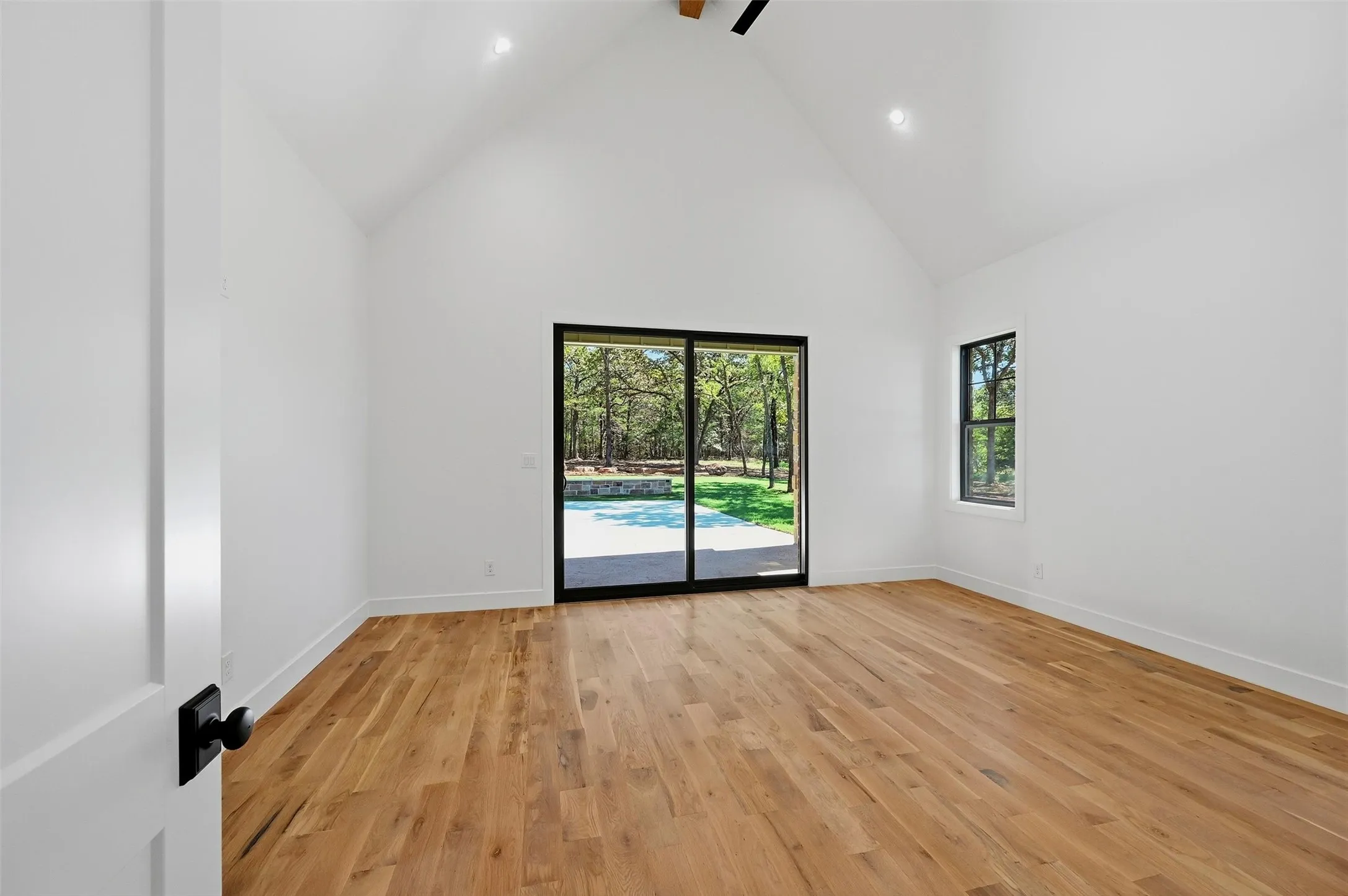 Vaulted ceiling with recessed lighting, wood-finish flooring, and a large sliding glass door