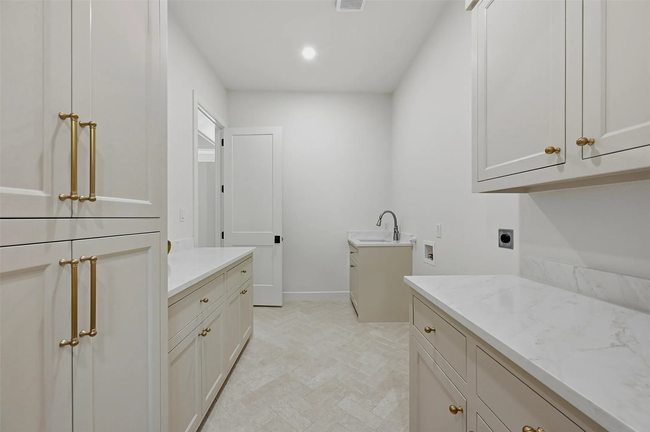Herringbone pattern tile flooring, white shaker-style cabinetry, light-toned countertops, and a utility sink with a high-arch faucet